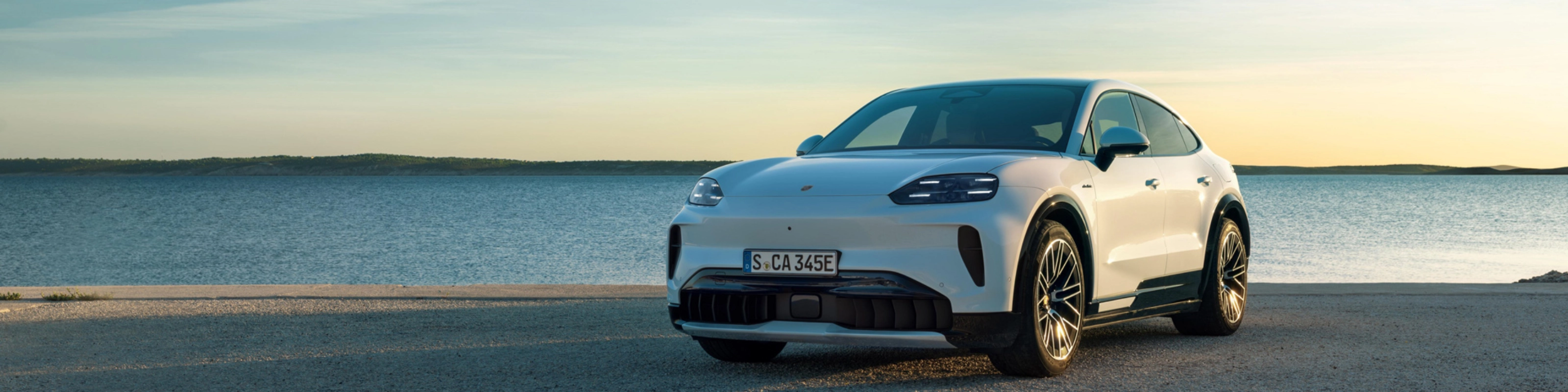 Weißer Porsche steht am Wasser bei Sonnenuntergang.