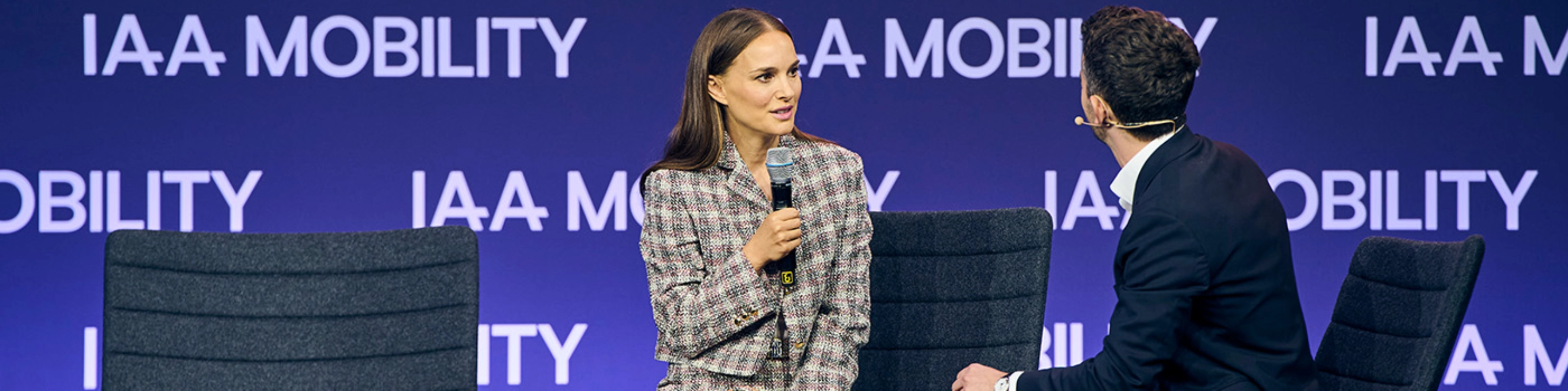 Natalie Portman bei einem Live-Bühneninterview auf der IAA Mobility, sitzend neben einem Moderator vor einer Bühne mit Veranstaltungslogo.