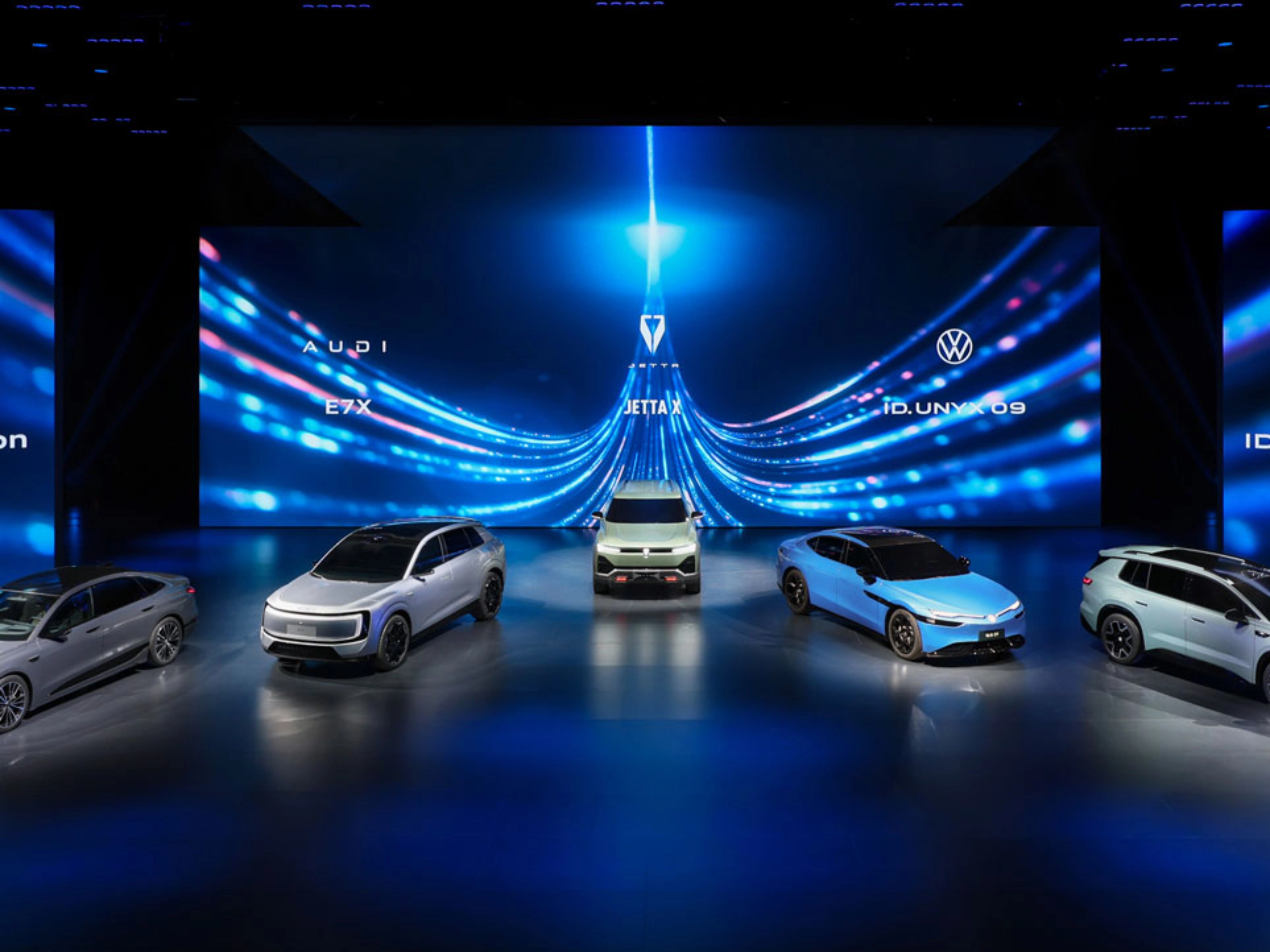 Five cars displayed on a stage with blue digital background.