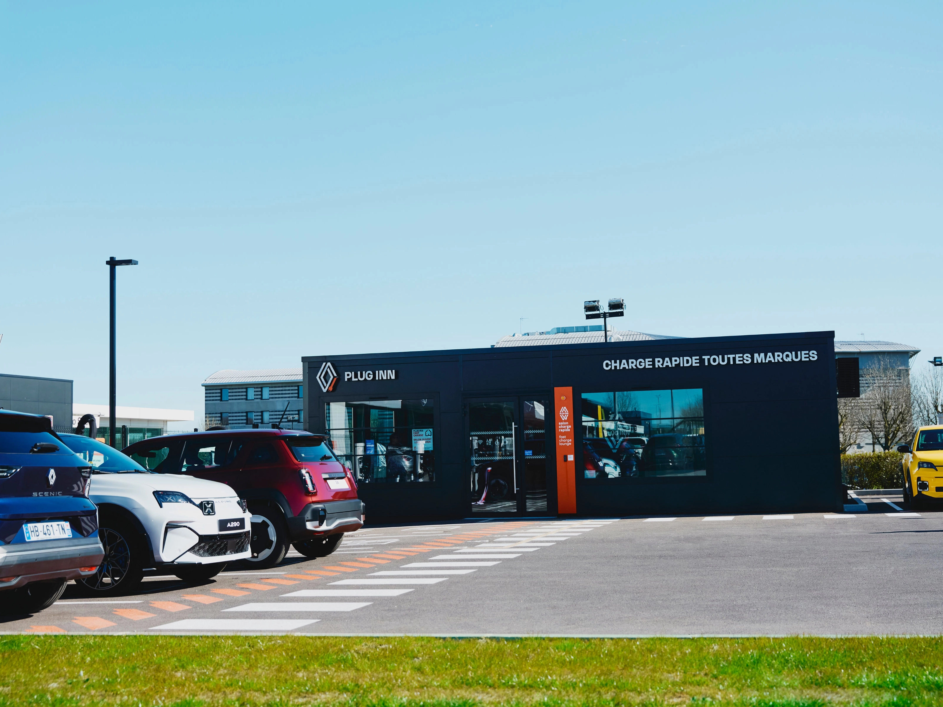 Außenansicht einer Plug-Inn-Schnellladestation mit mehreren geparkten Autos.