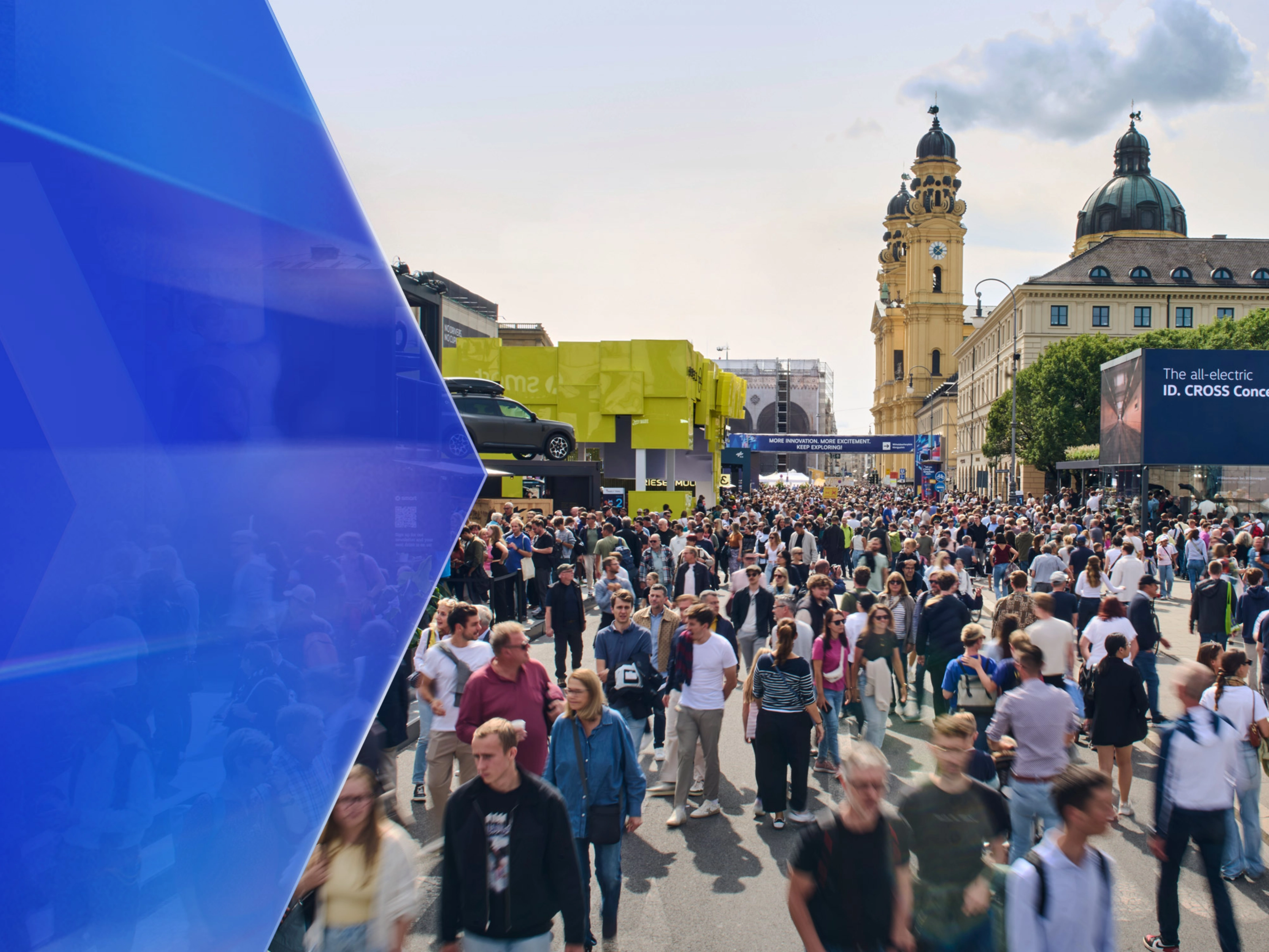 Große Menschenmenge auf einer Mobilitätsmesse im Freien mit Ausstellungsständen und Altbauten.
