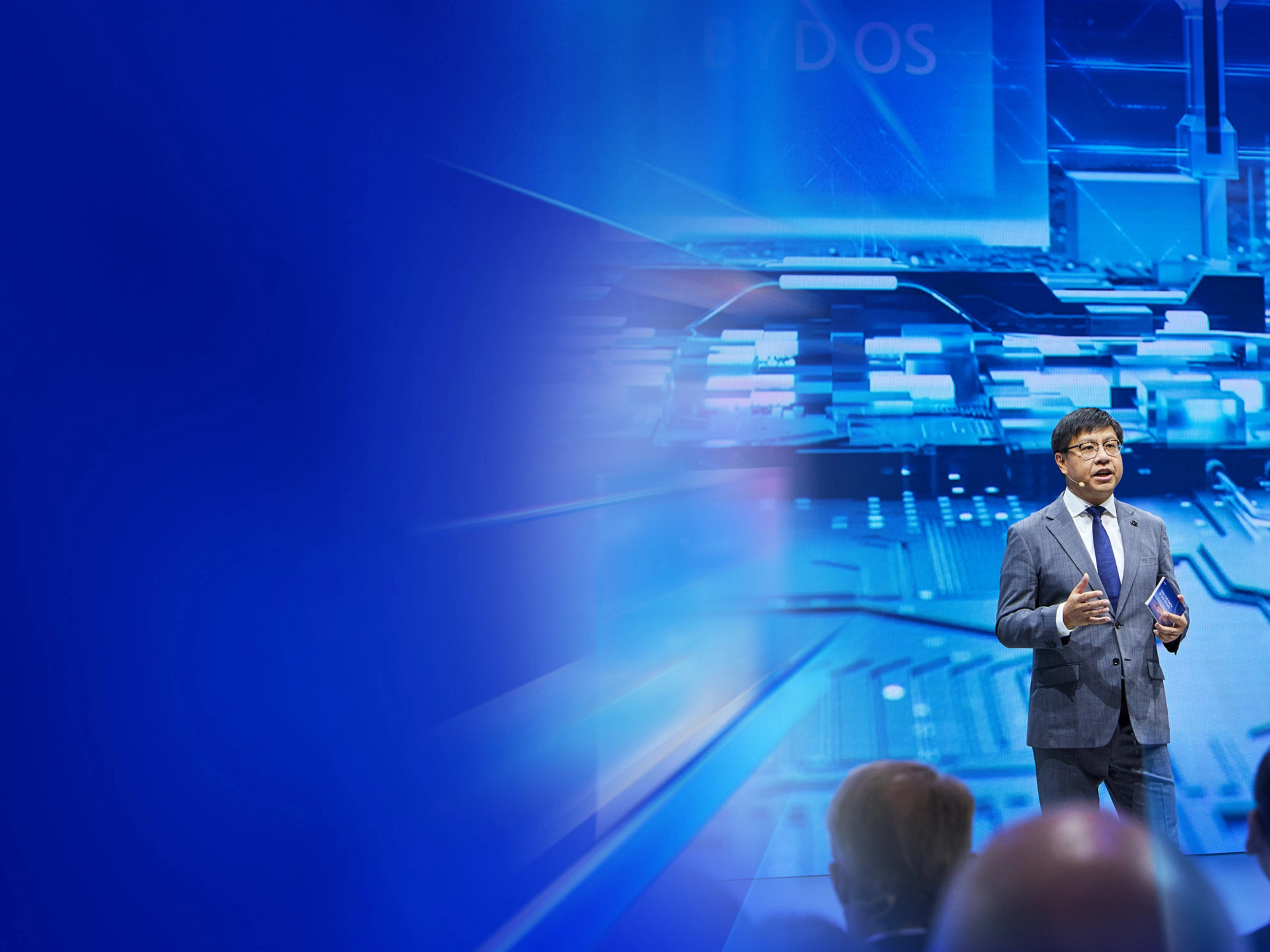 Ein Redner im Anzug spricht auf der IAA Summit Bühne vor digitalem Schaltkreis-Hintergrund.