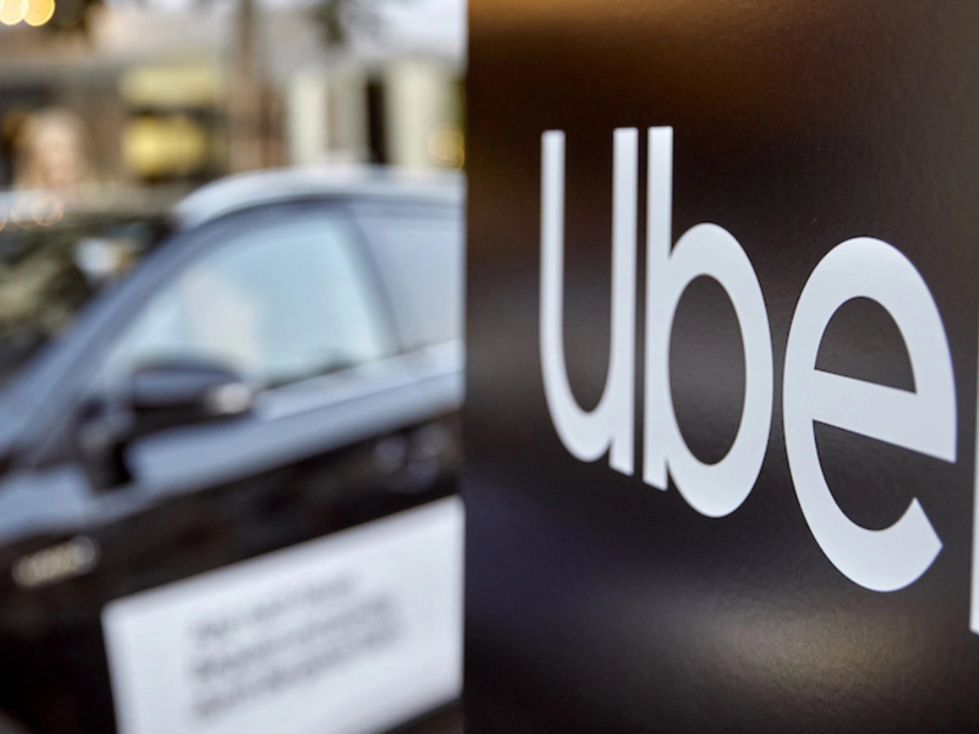 Uber-Logo auf einem Schild, dahinter unscharf ein Auto.