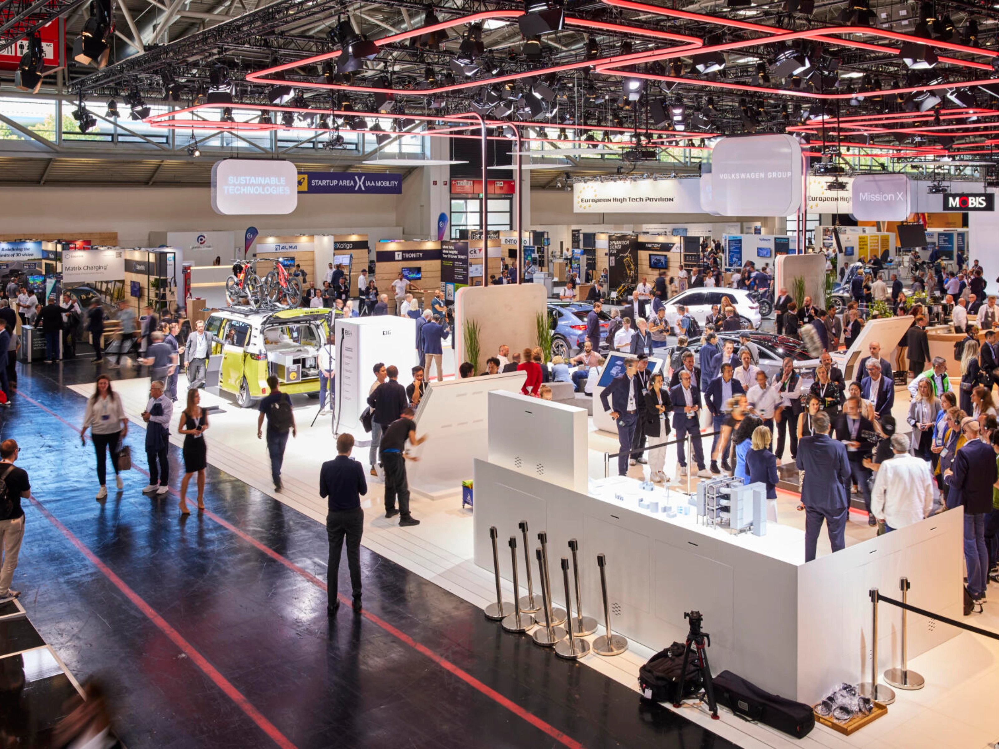 Busy exhibition hall at IAA Mobility 2023 featuring multiple booths, vehicles, and technology displays, with many visitors engaging and walking through the space.