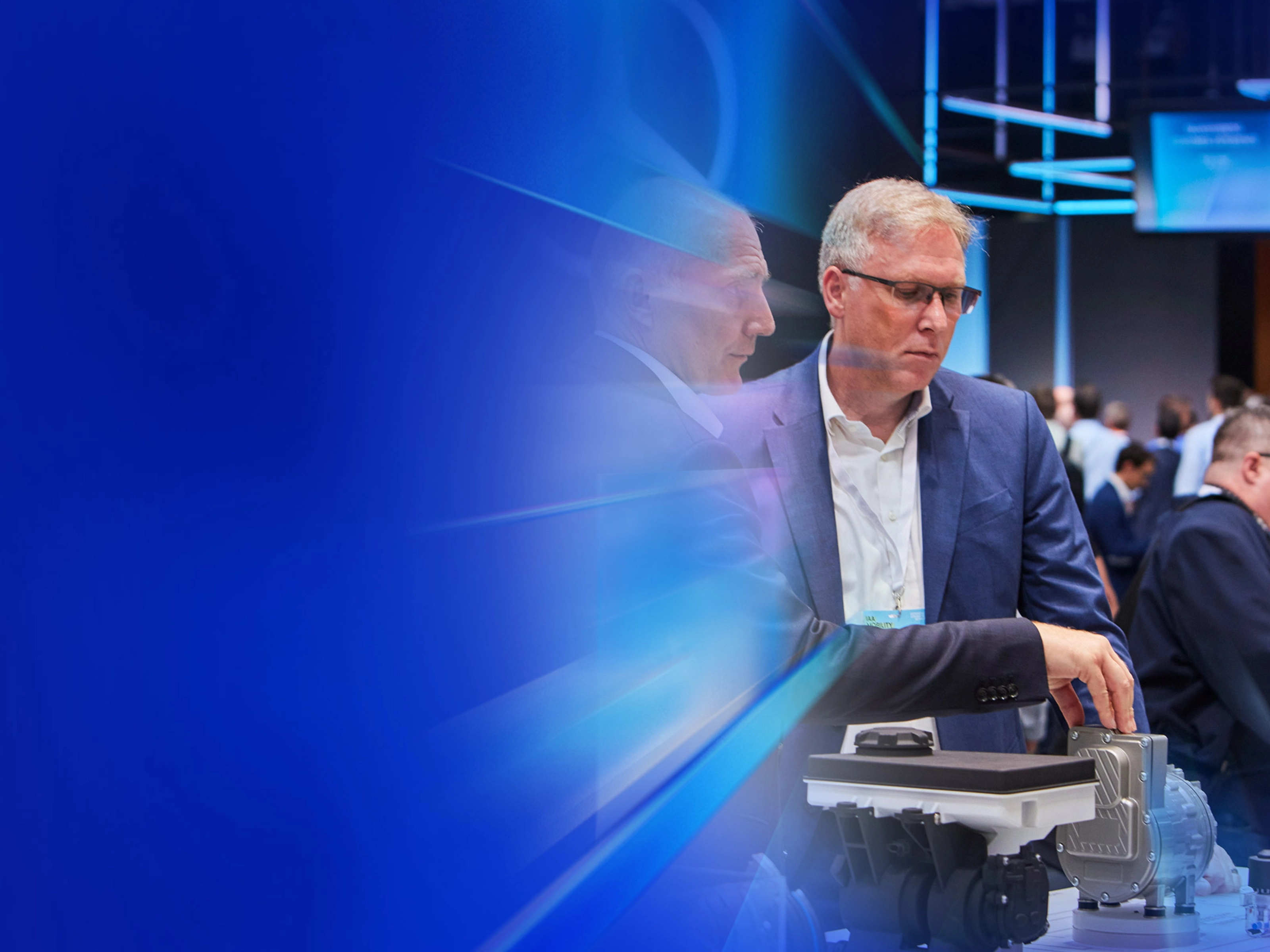 Drei Männer begutachten ein technisches Bauteil auf einer Messe beim IAA Summit.