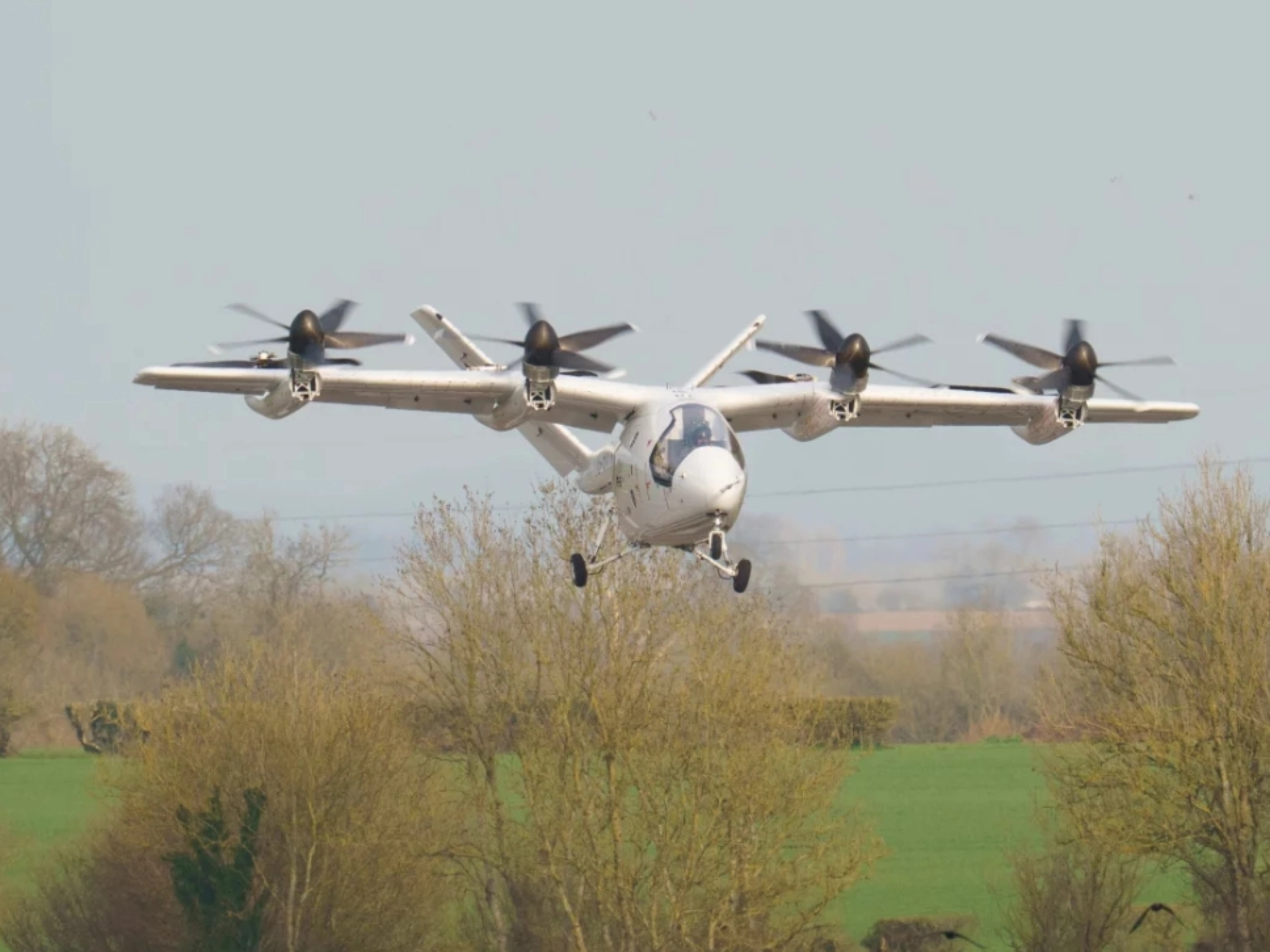 Electric aircraft with multiple rotors flying over trees.