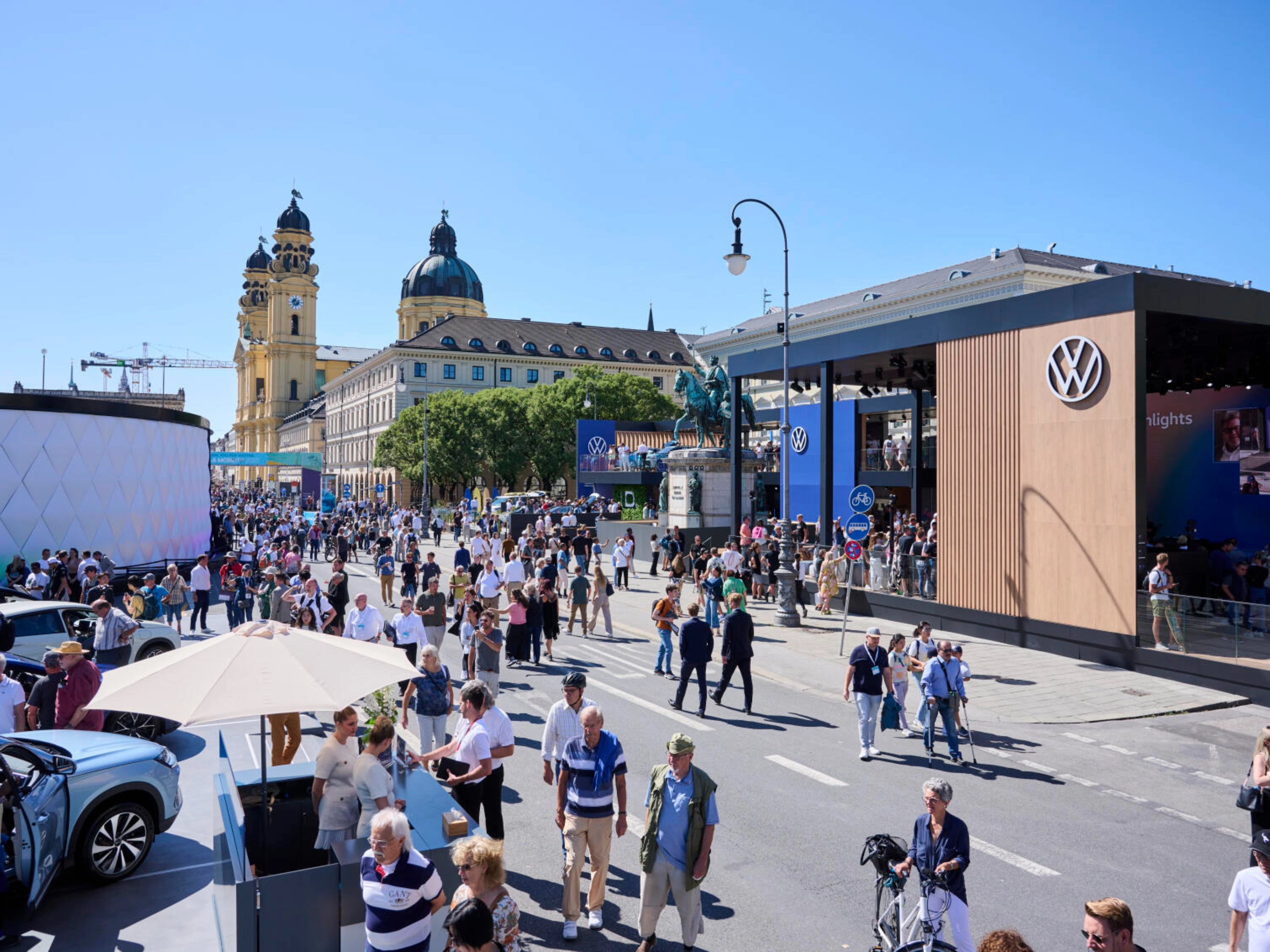 Menschen besuchen eine Outdoor-Mobilitätsmesse mit Ständen und historischen Gebäuden.