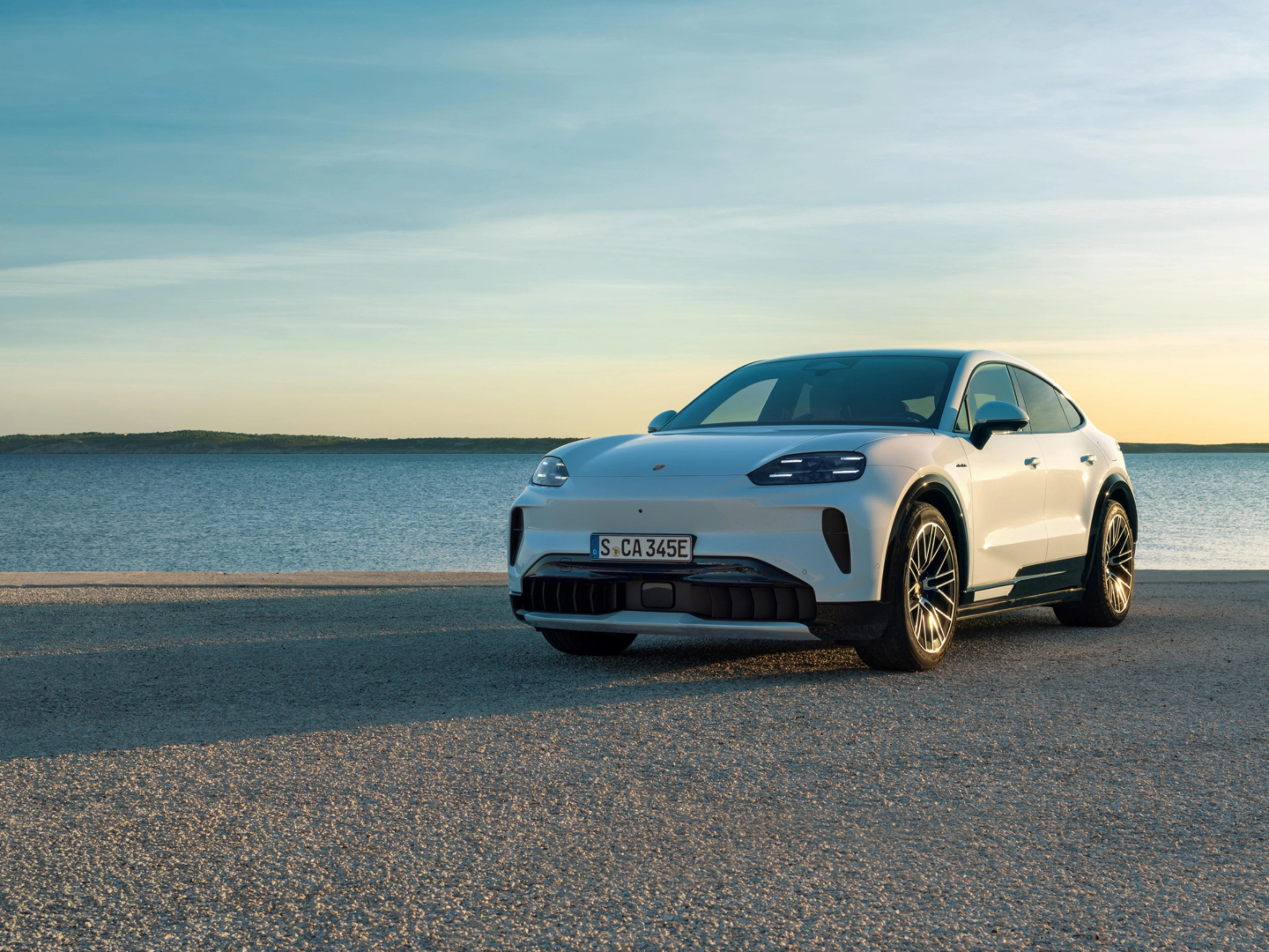 Weißer Porsche steht am Wasser bei Sonnenuntergang.