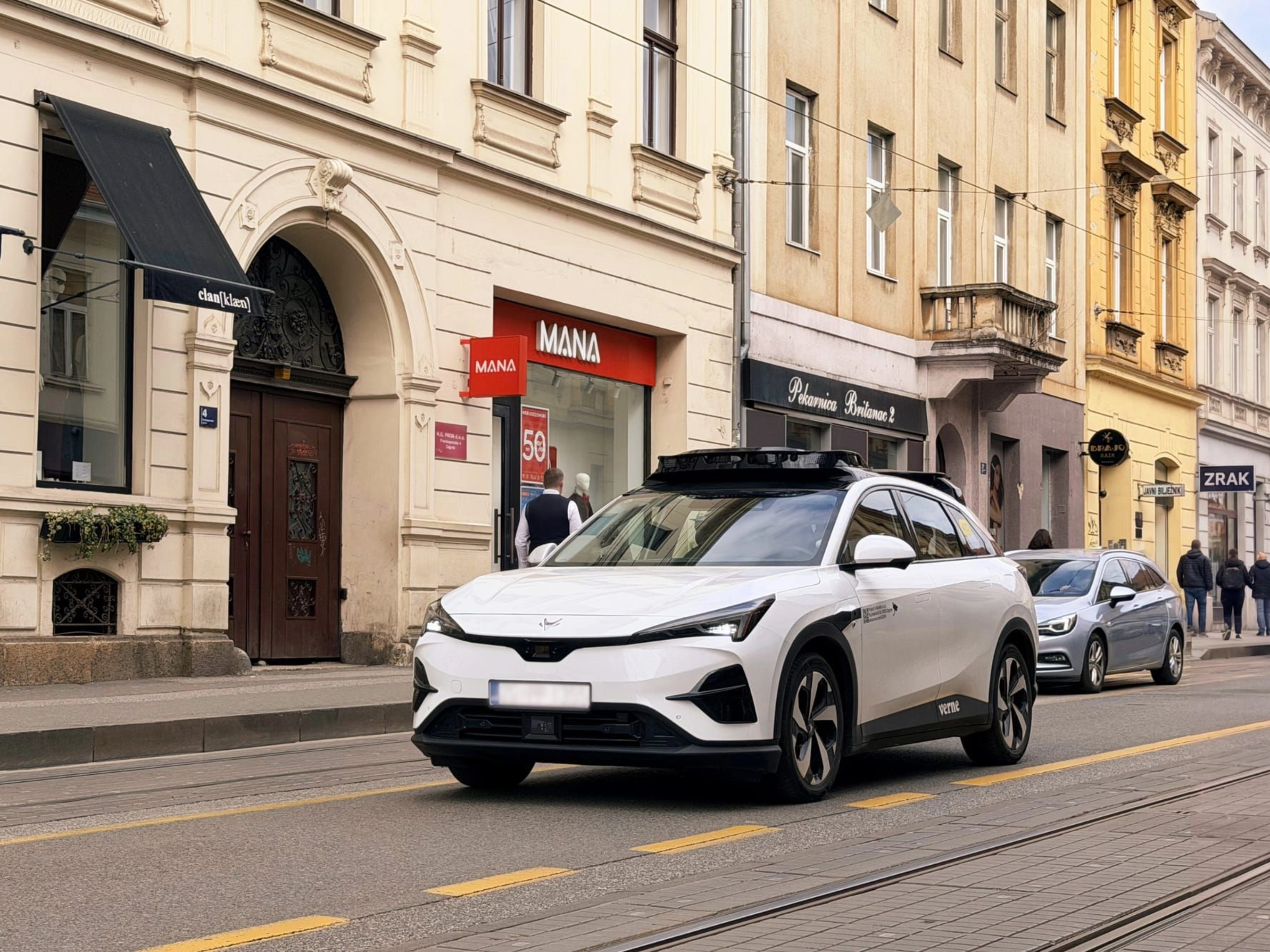 Autonomes Testfahrzeug fährt durch eine Stadtstraße mit Geschäften
