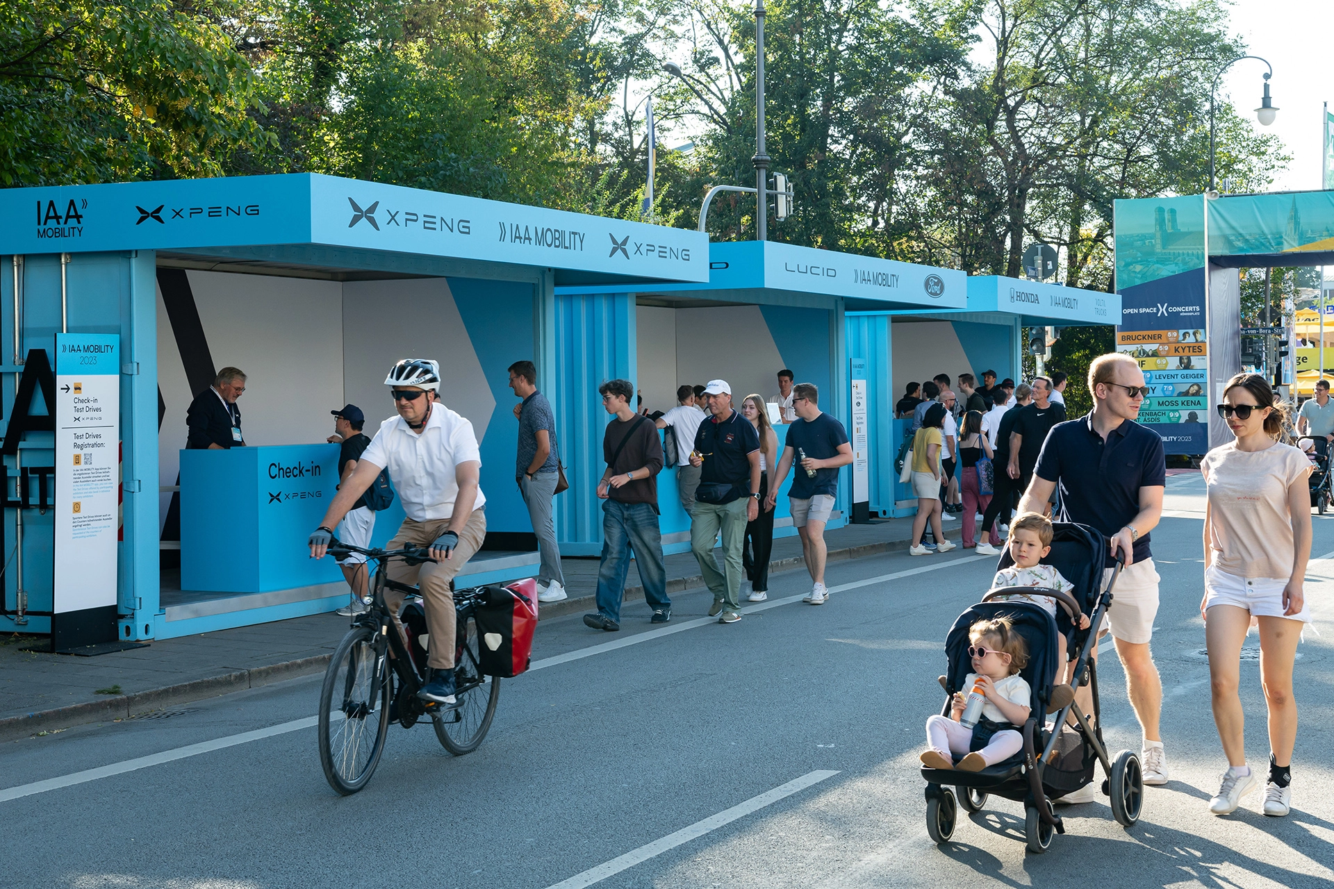 Menschen gehen und fahren mit dem Fahrrad an IAA Mobility Check-in-Ständen auf einer gesperrten Straße vorbei.