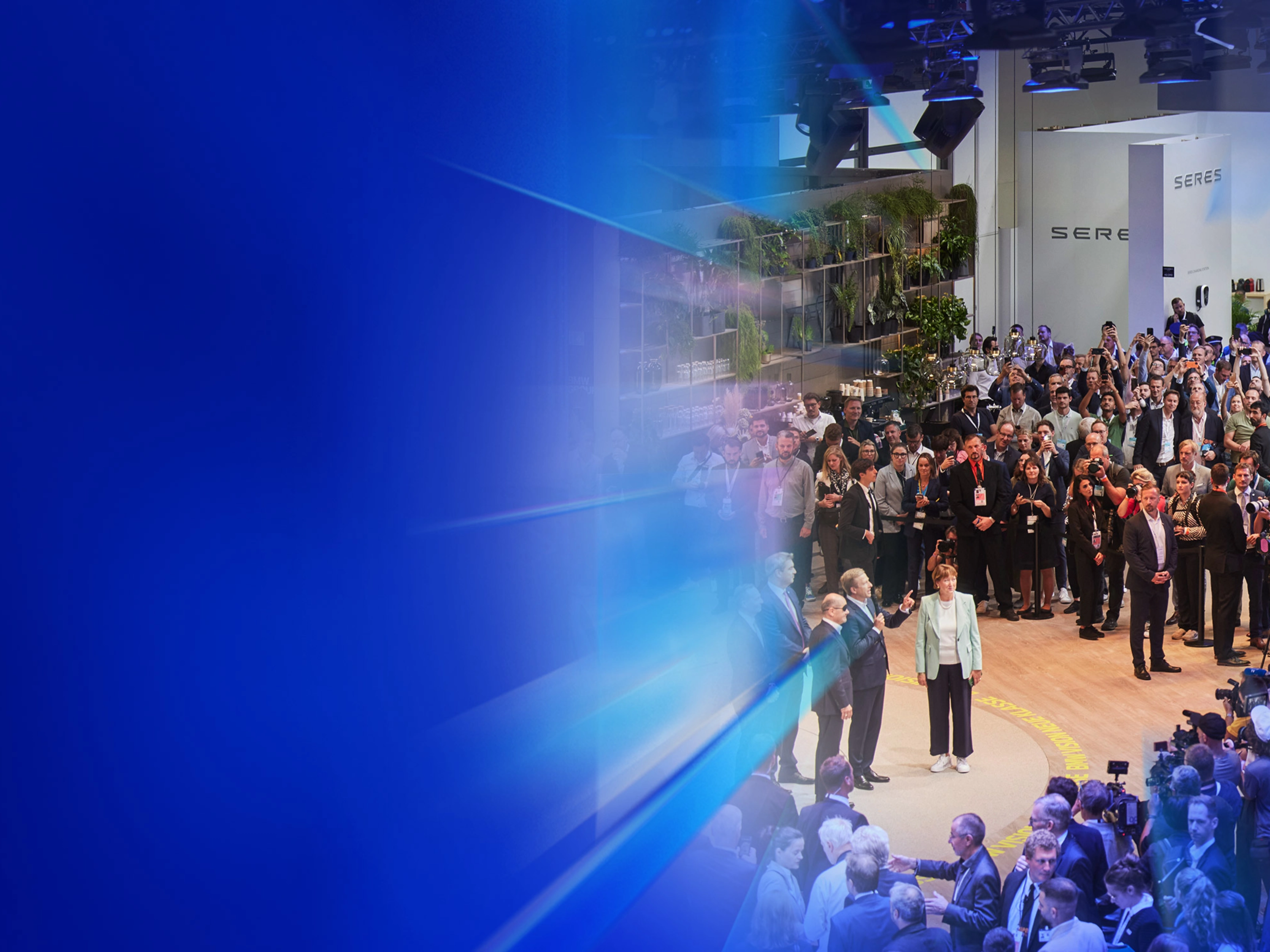 Menschenmenge und Presse auf einer Autoausstellung mit dem Text „5 Gründe – IAA Summit“.
