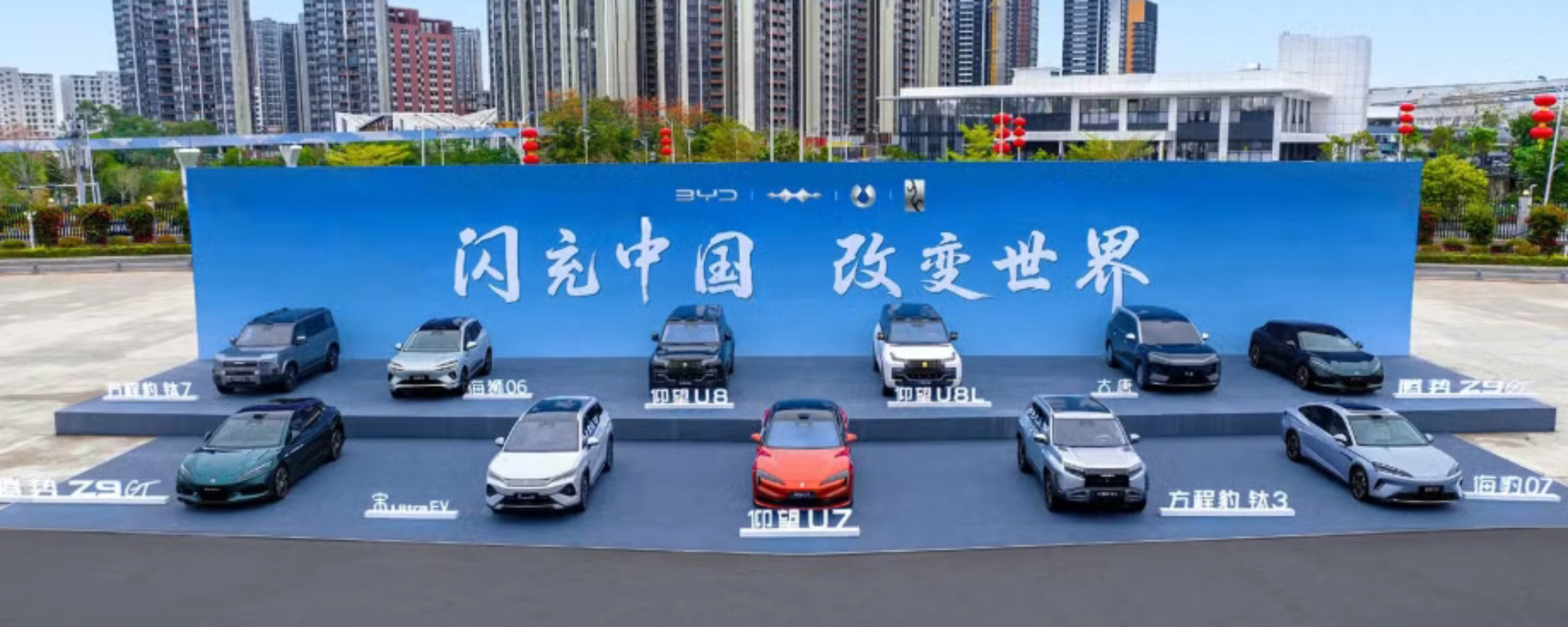 BYD vehicles displayed on a stage outdoors in front of a large promotional backdrop.