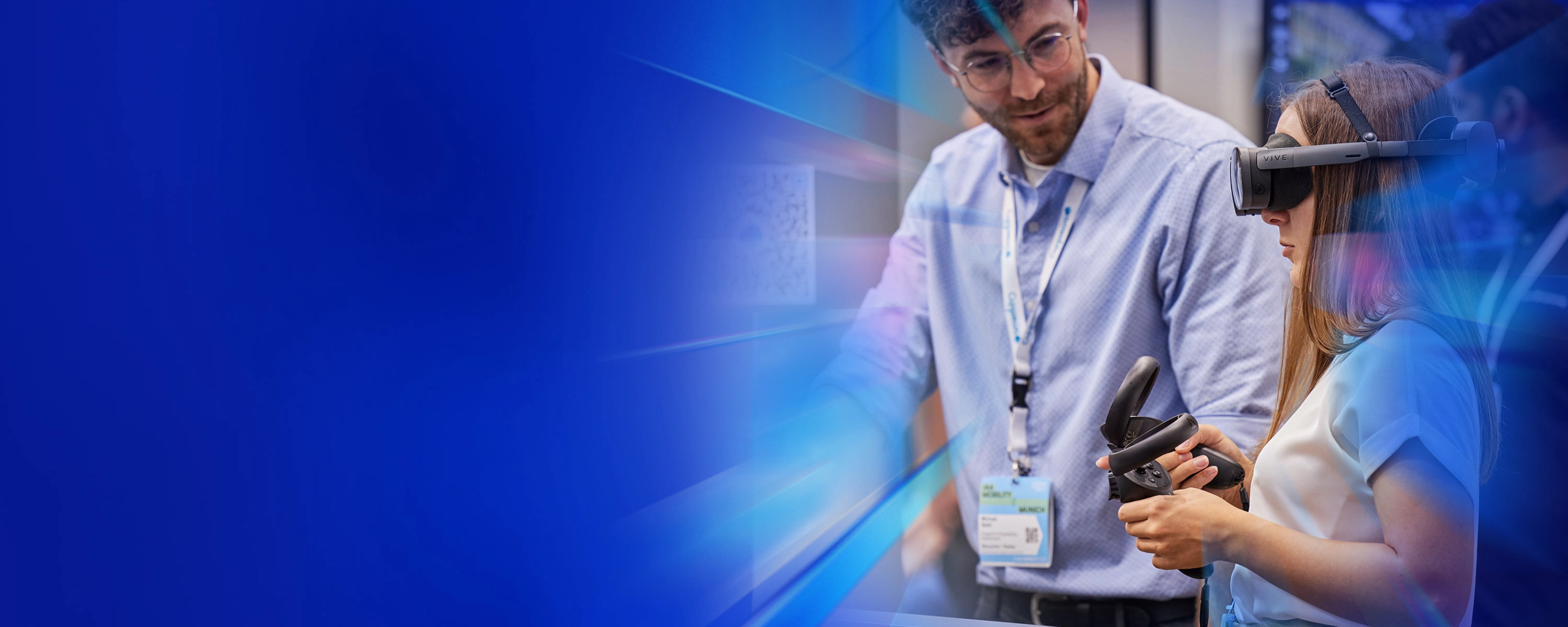Frau testet VR-Brille mit Controller, daneben steht ein Mann an einem Messestand.