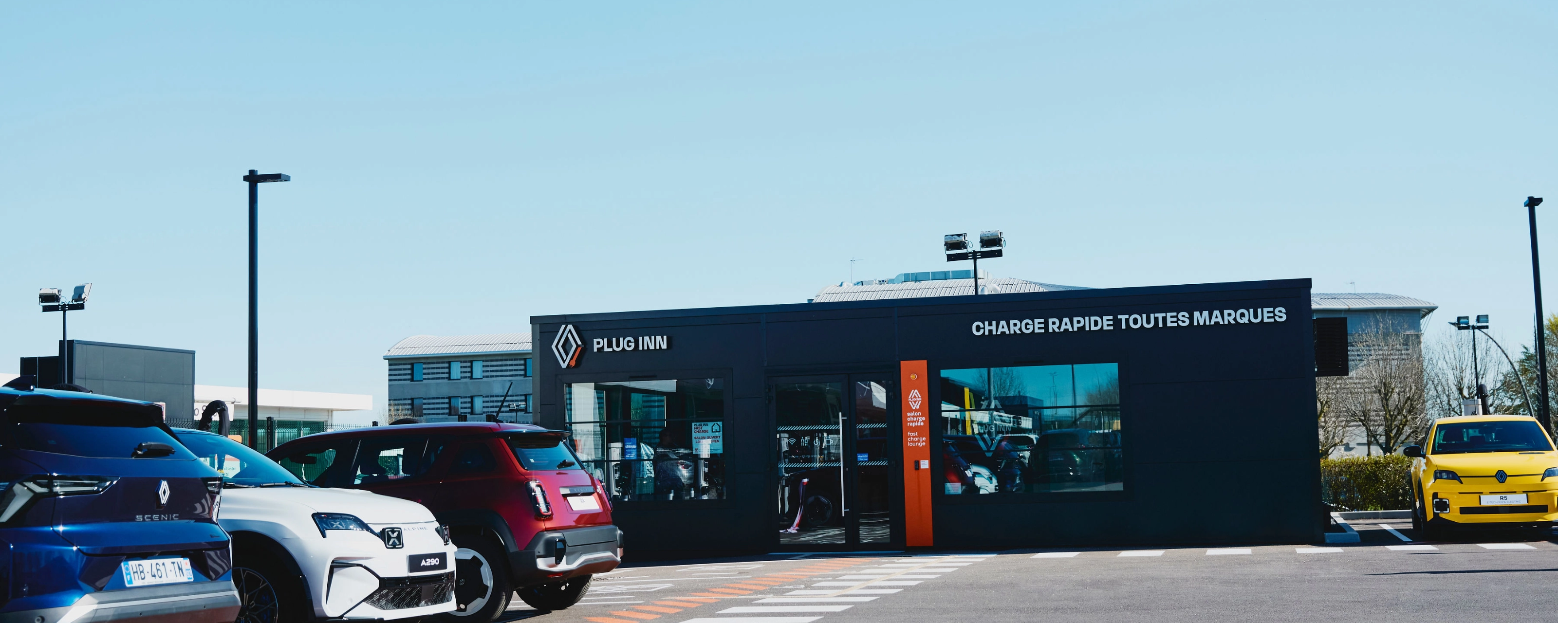 Außenansicht einer Plug-Inn-Schnellladestation mit mehreren geparkten Autos.