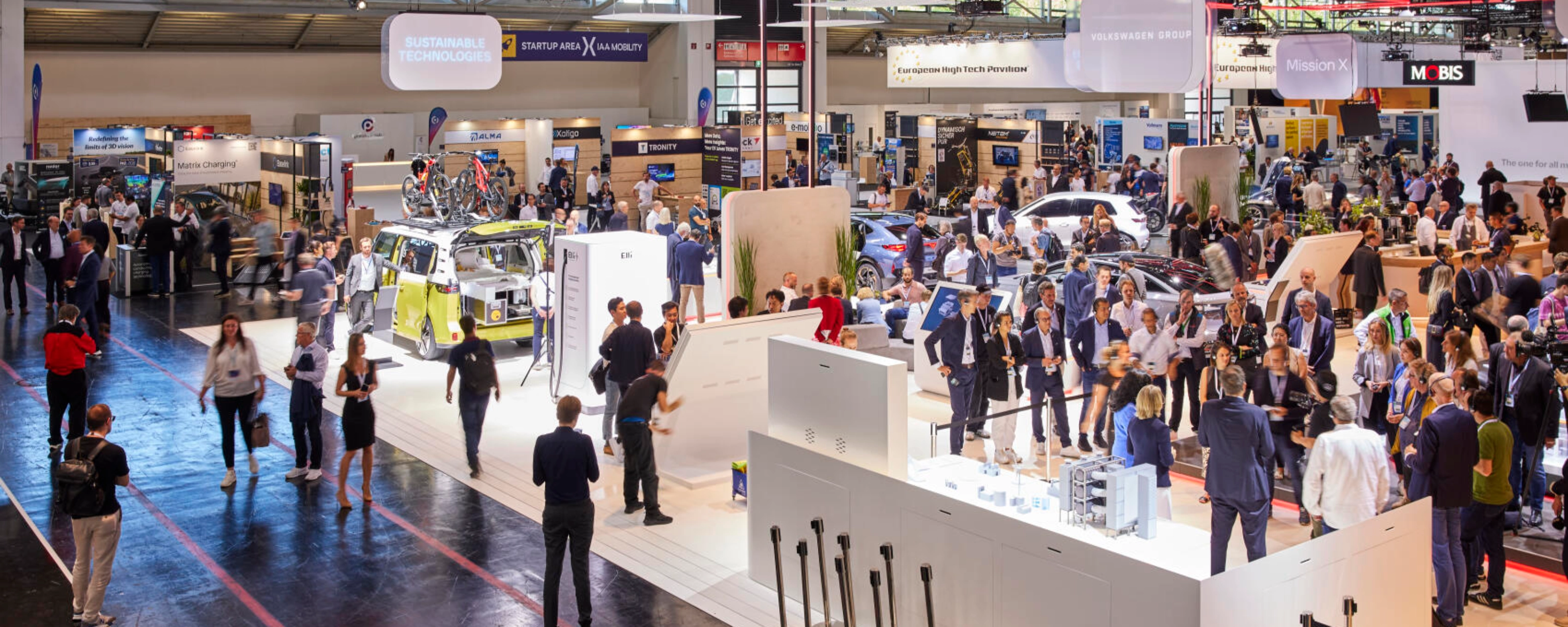 Busy exhibition hall at IAA Mobility 2023 featuring multiple booths, vehicles, and technology displays, with many visitors engaging and walking through the space.