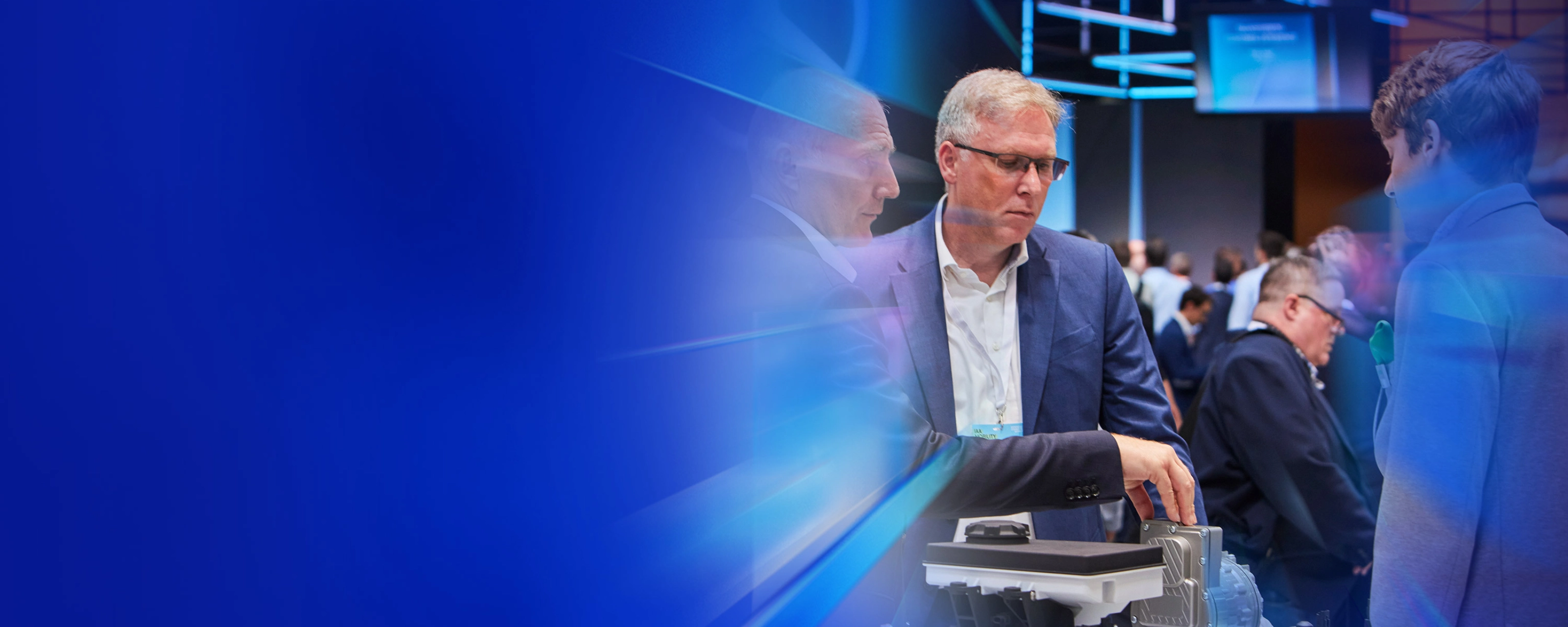 Drei Männer begutachten ein technisches Bauteil auf einer Messe beim IAA Summit.
