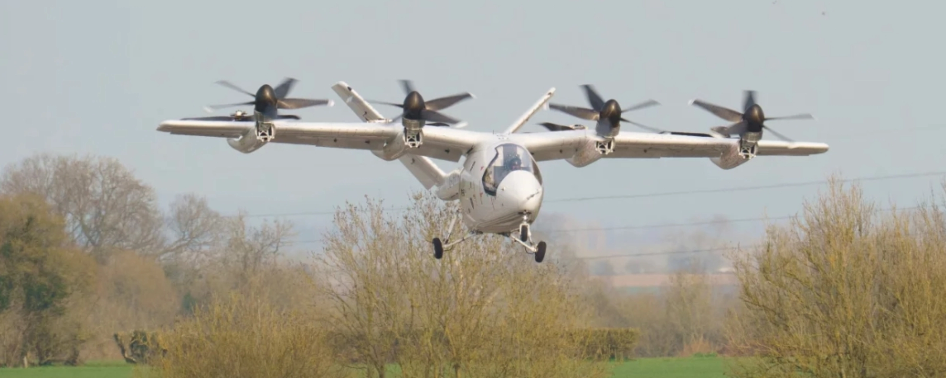 Electric aircraft with multiple rotors flying over trees.