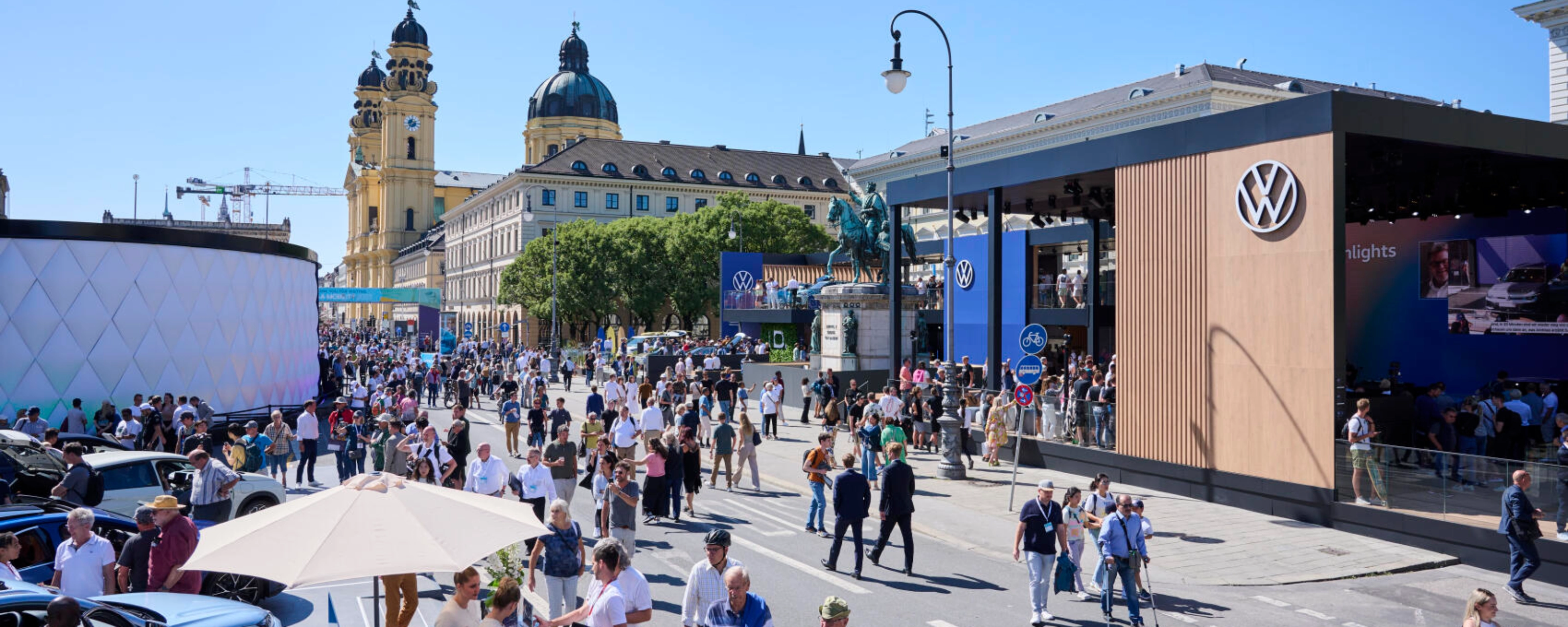 Menschen besuchen eine Outdoor-Mobilitätsmesse mit Ständen und historischen Gebäuden.