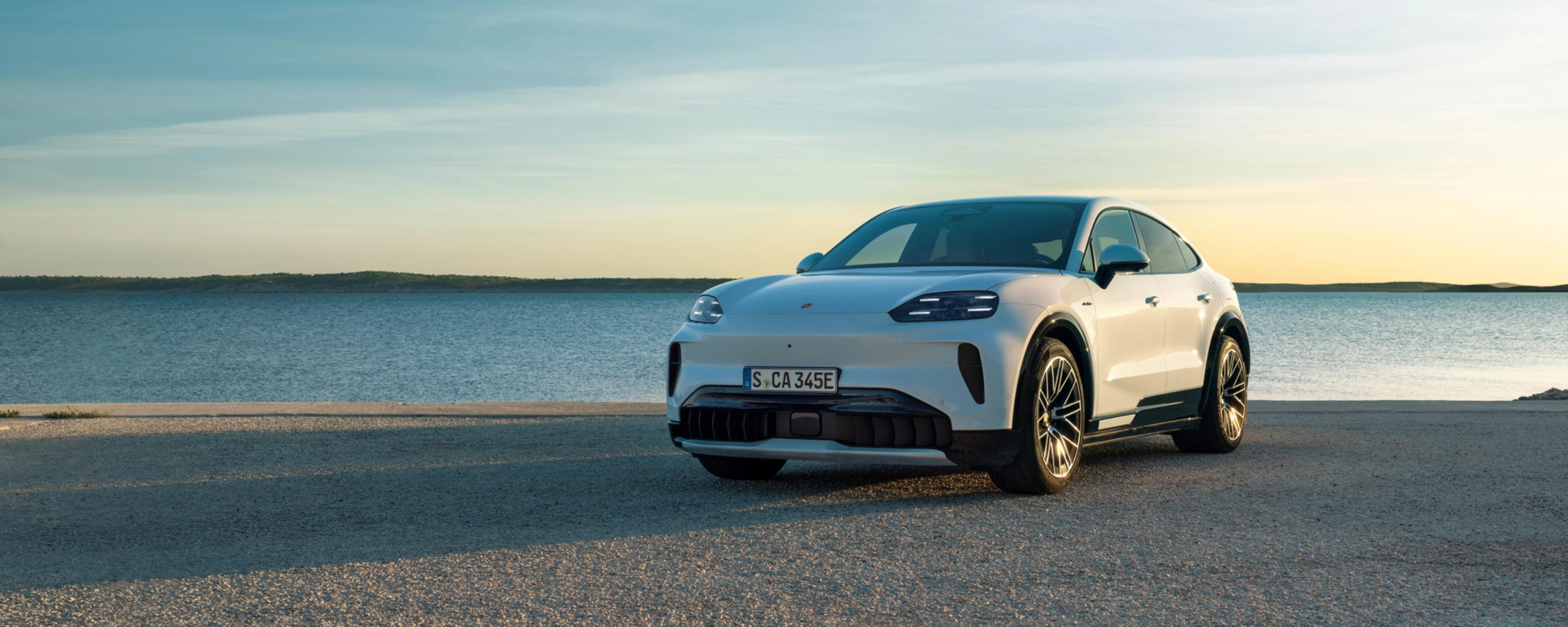 Weißer Porsche steht am Wasser bei Sonnenuntergang.