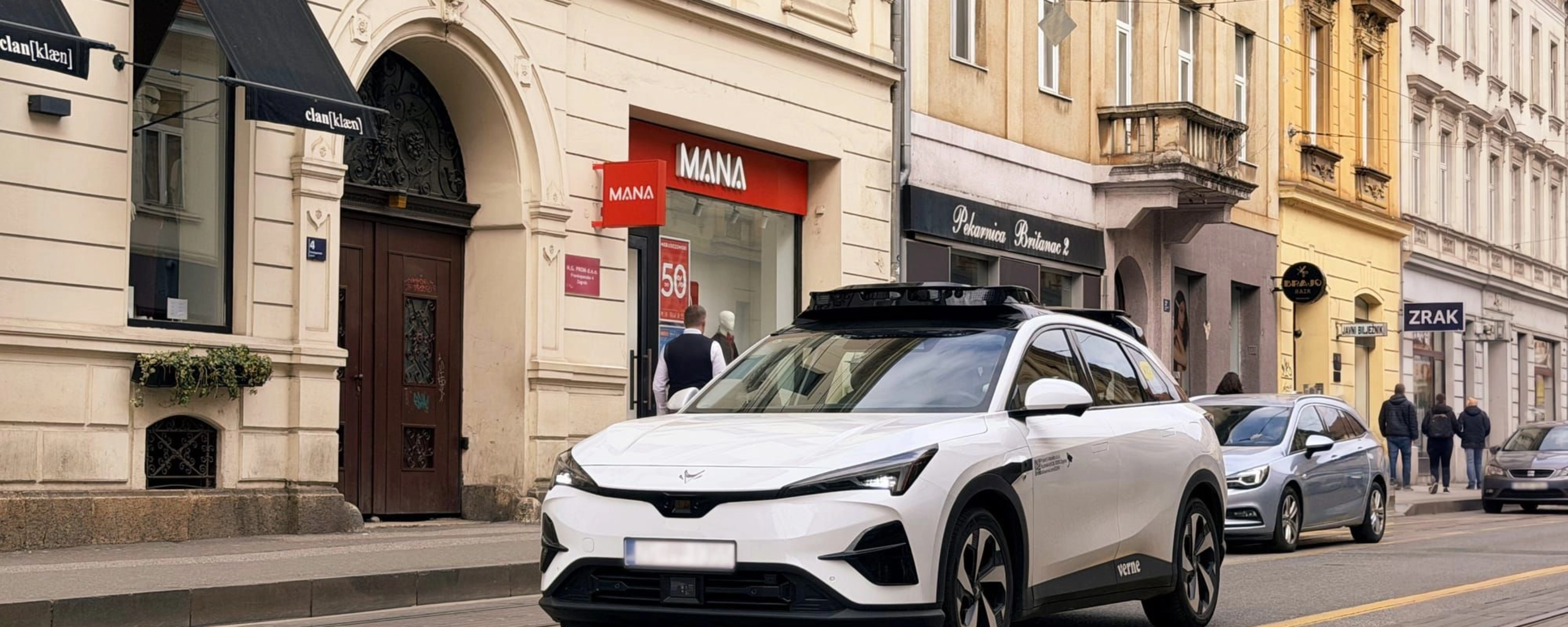 Autonomes Testfahrzeug fährt durch eine Stadtstraße mit Geschäften