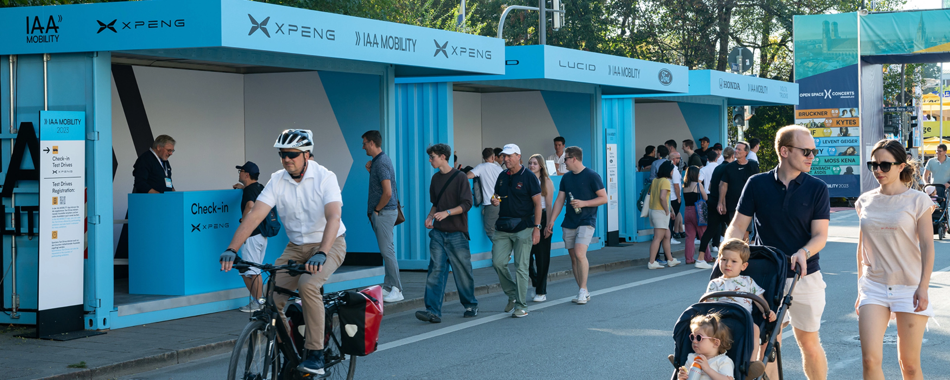Menschen gehen und fahren mit dem Fahrrad an IAA Mobility Check-in-Ständen auf einer gesperrten Straße vorbei.