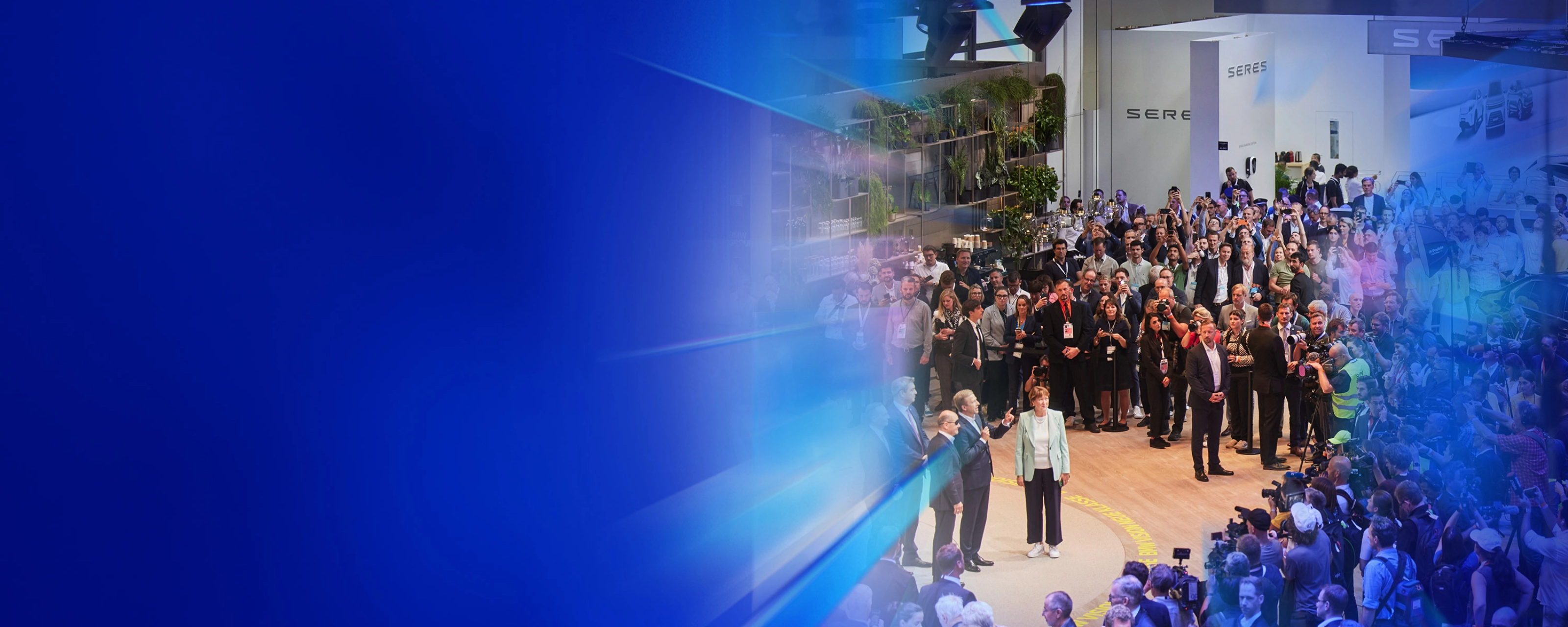 Menschenmenge und Presse auf einer Autoausstellung mit dem Text „5 Gründe – IAA Summit“.