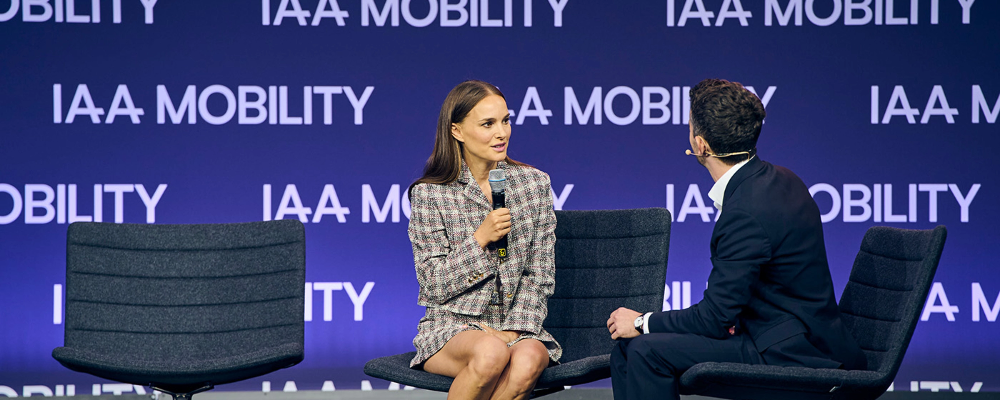 Natalie Portman bei einem Live-Bühneninterview auf der IAA Mobility, sitzend neben einem Moderator vor einer Bühne mit Veranstaltungslogo.
