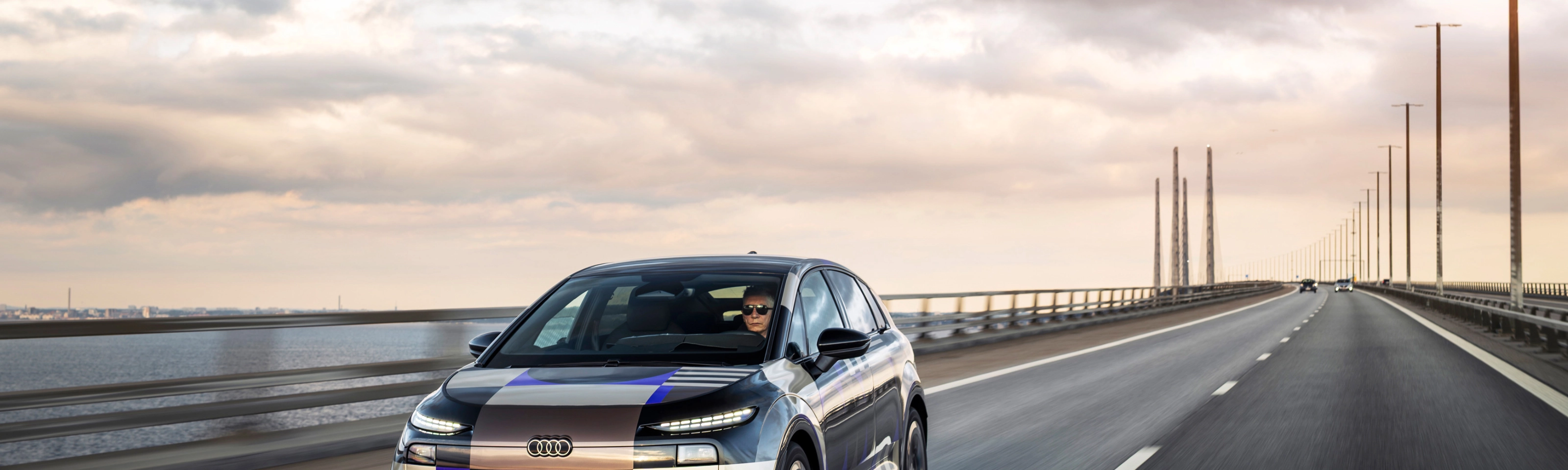Audi prototype electric vehicle driving on an open road at sunset.