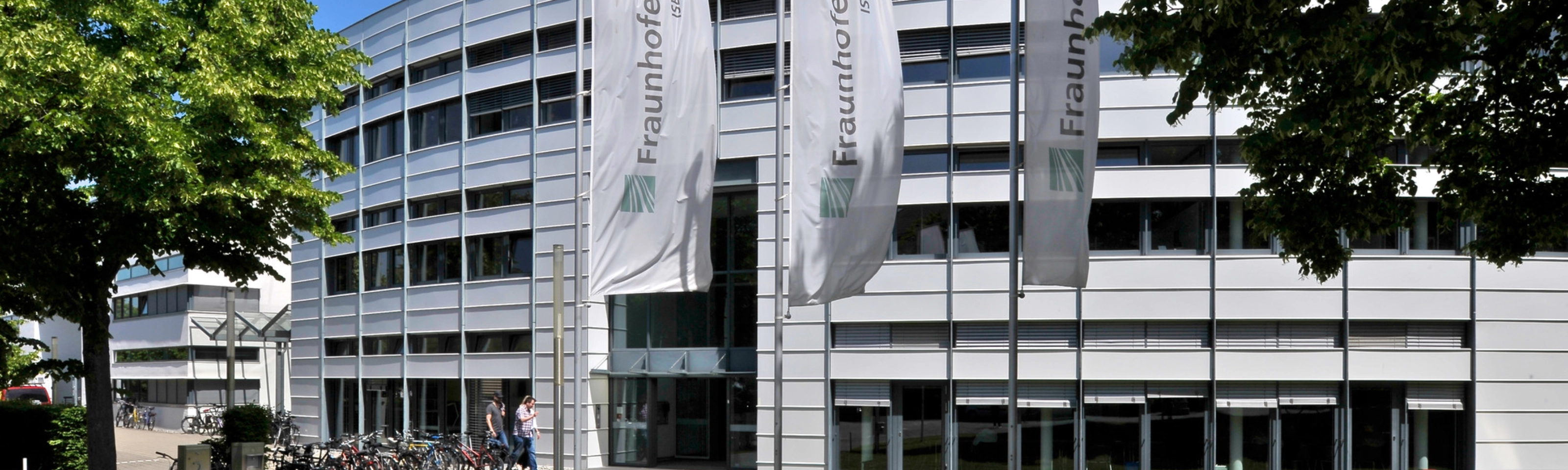 Modernes Fraunhofer-Institutsgebäude mit Fahnen und Bäumen davor.