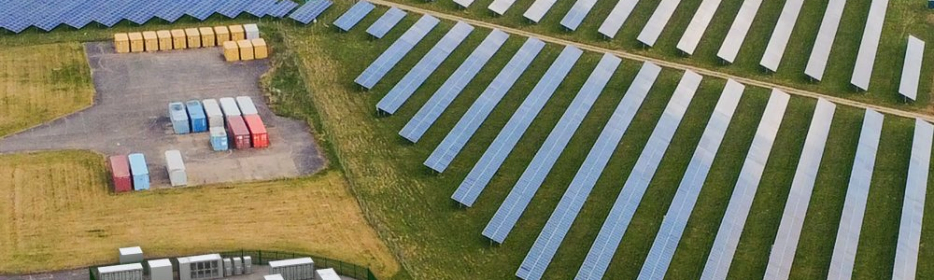 Luftaufnahme einer Solaranlage mit Reihen von Solarpaneelen und mehreren Containern.