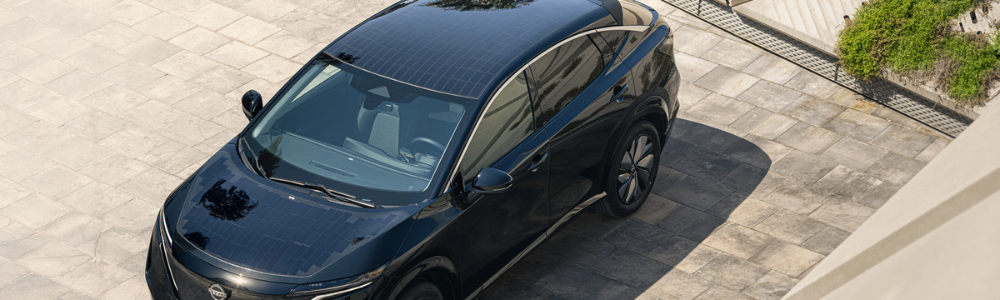 Ein schwarzes Elektro-SUV von Nissan steht auf einer gepflasterten Fläche im Sonnenlicht.