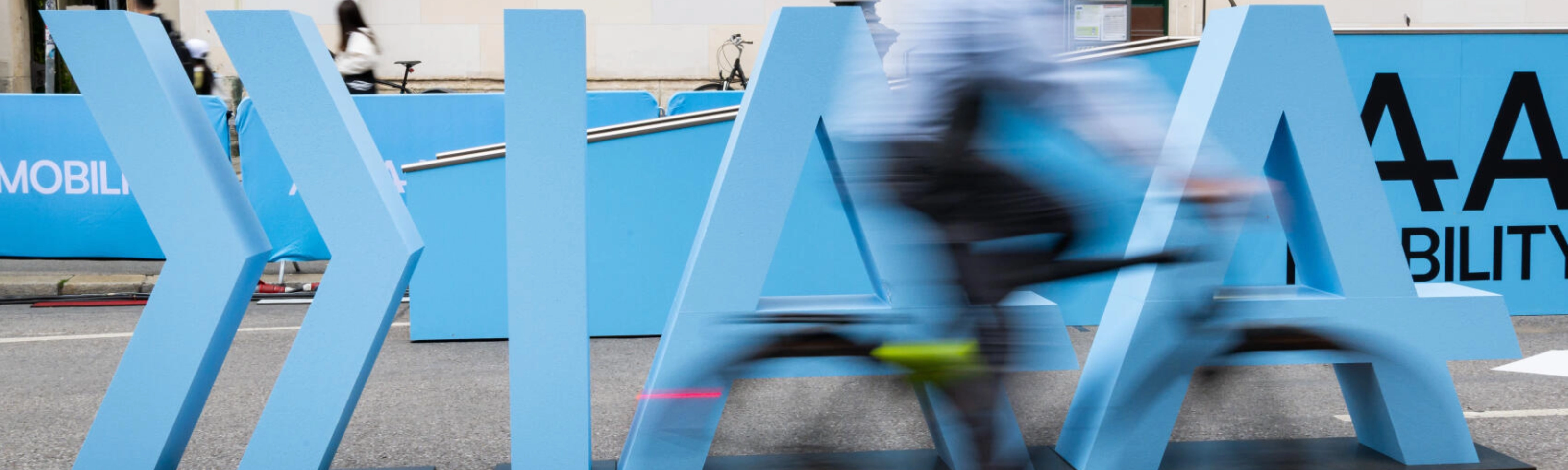 Cyclist rides past large IAA Mobility lettering on a city street.