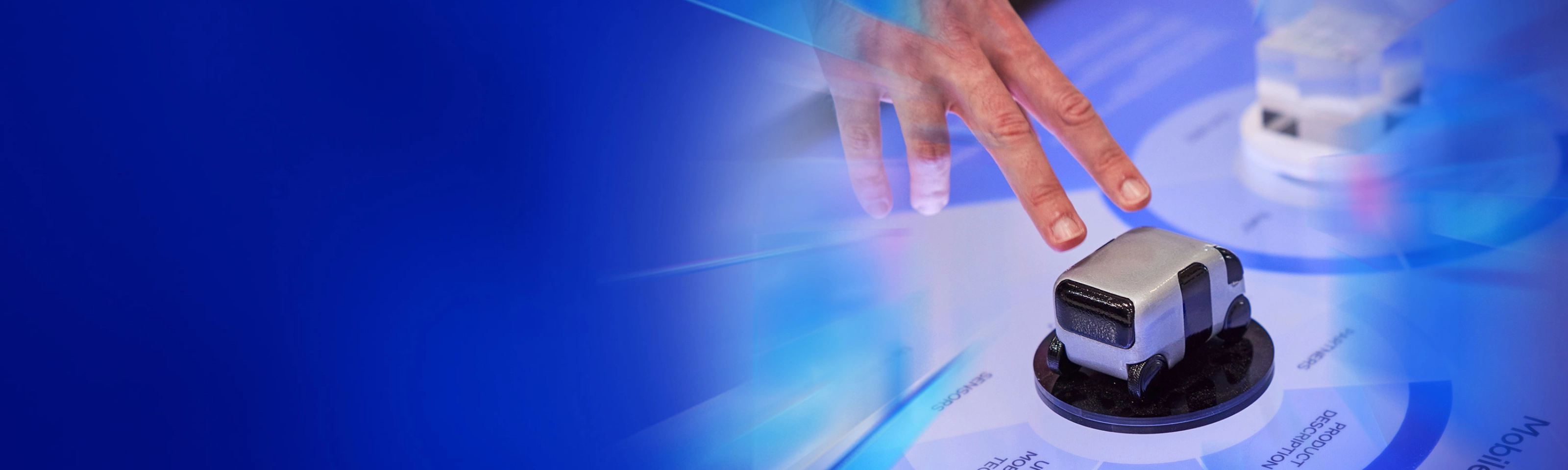 Eine Hand interagiert mit einem kleinen Fahrzeugmodell auf einer digitalen Fläche beim IAA Summit.