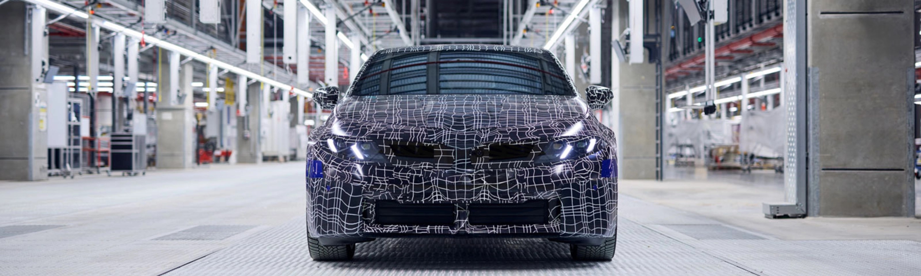 Ein getarntes Auto-Prototyp steht in einer hell beleuchteten Fahrzeugproduktionshalle.