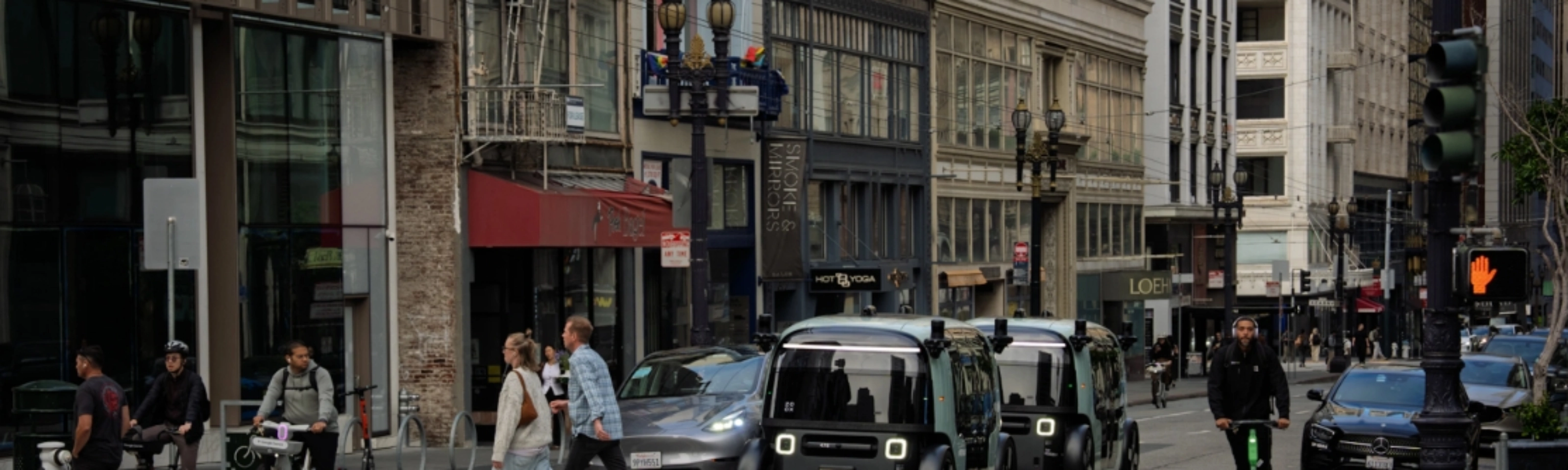 Zoox autonomous shuttle driving through a city intersection with pedestrians nearby.