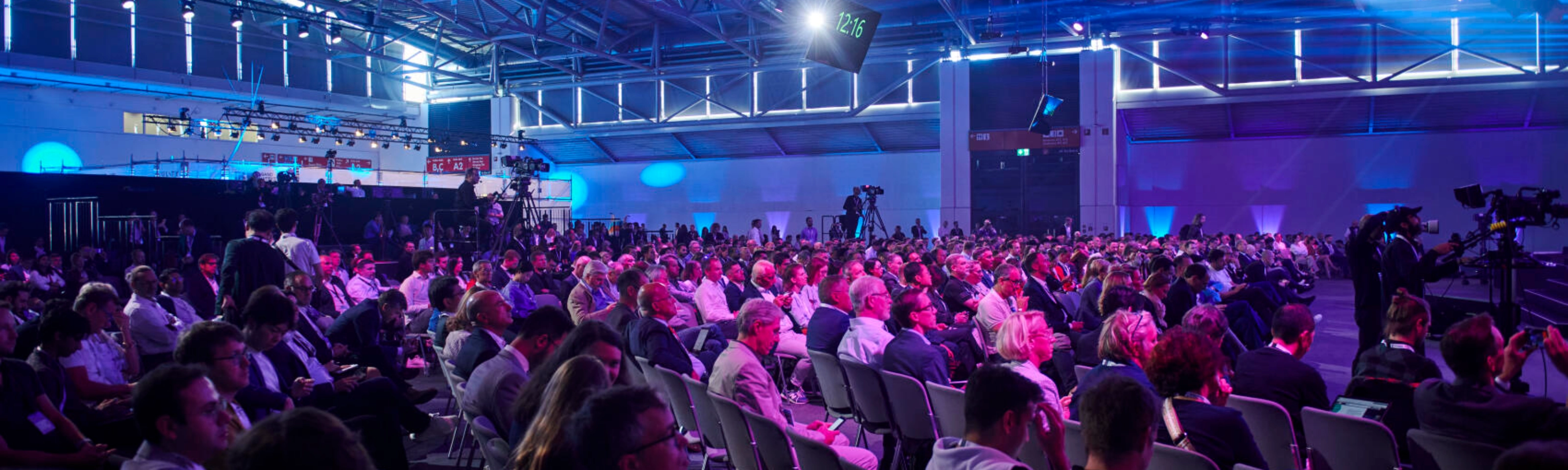 Großes Publikum in einem Konferenzsaal bei der IAA MOBILITY mit Bühnenlicht und Kameras.