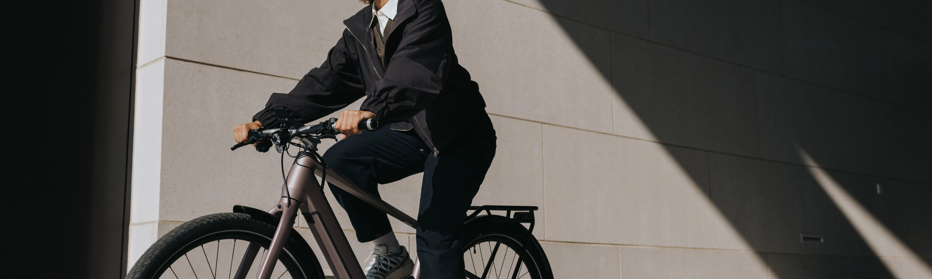 Person mit Helm fährt ein E-Bike neben einem modernen Gebäude.