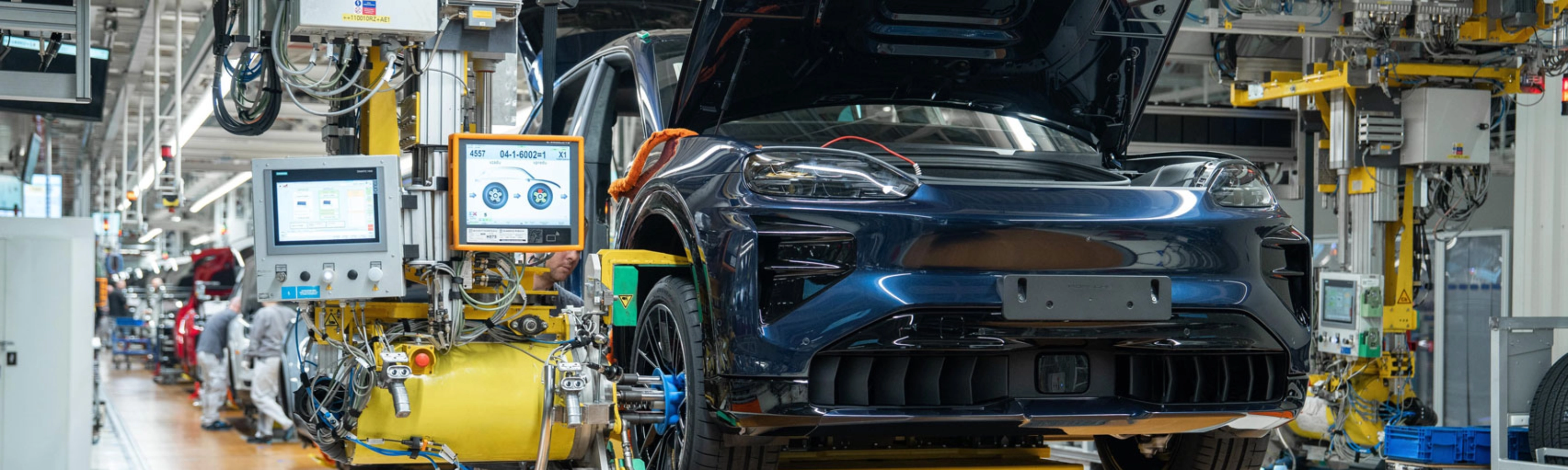 Teilmontiertes Elektroauto auf dem Montageband mit offenem Kofferraum und Maschinen ringsum.