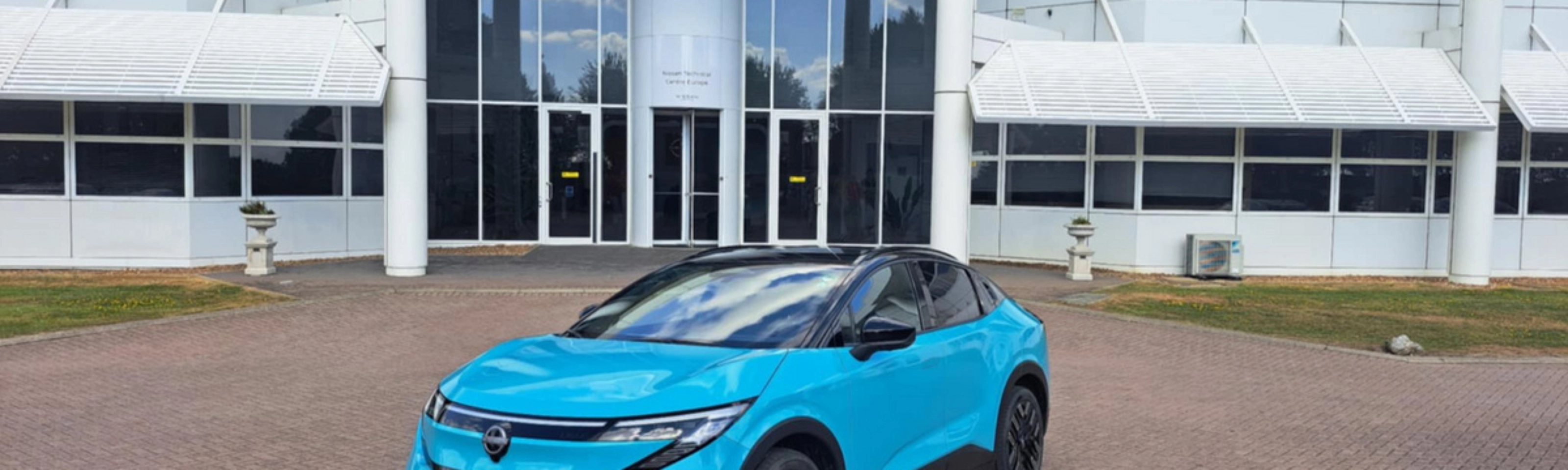 Blauer Nissan Crossover steht vor einem modernen Gebäude mit Glasfassade.