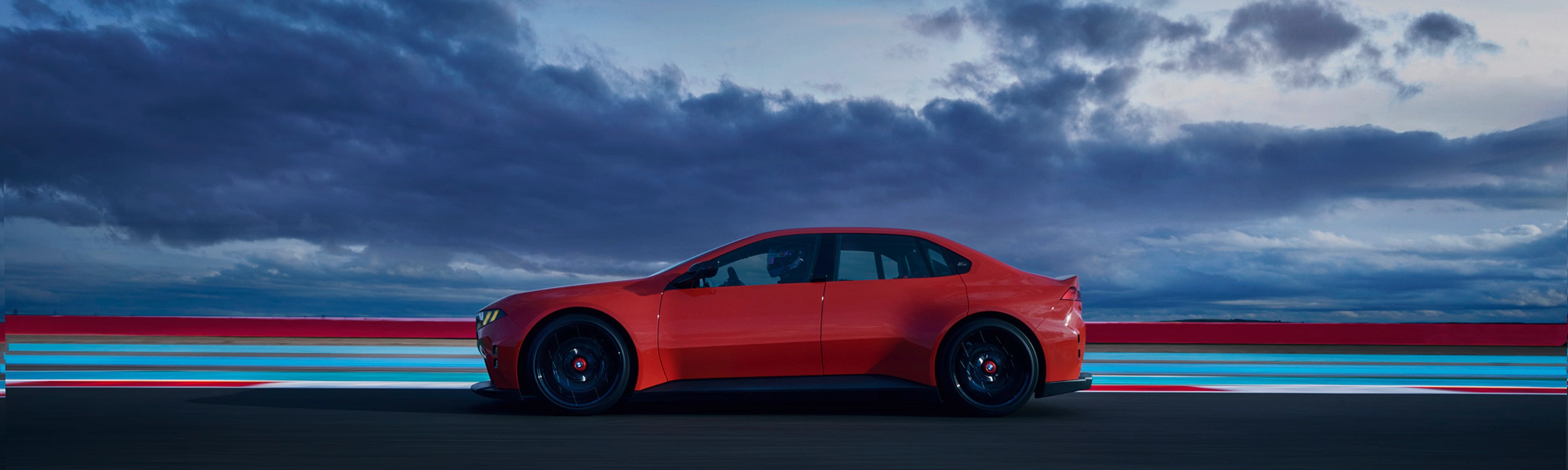 Red car driving on a road at dusk with clouds in the background.