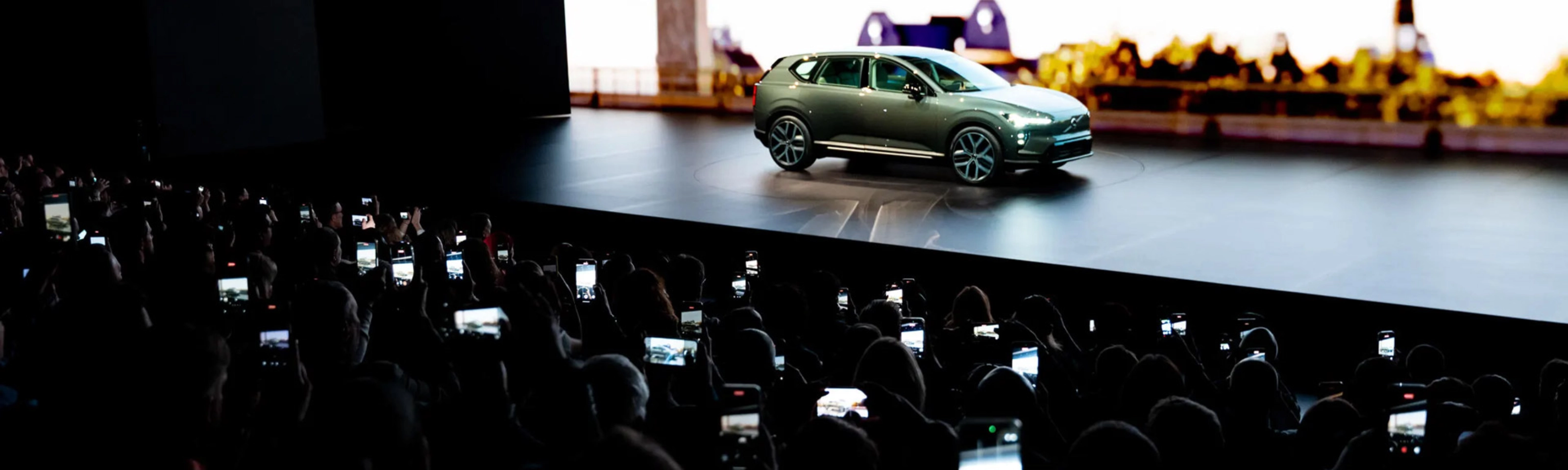 Elektrischer SUV wird auf einer Bühne präsentiert, das Publikum fotografiert mit Smartphones.