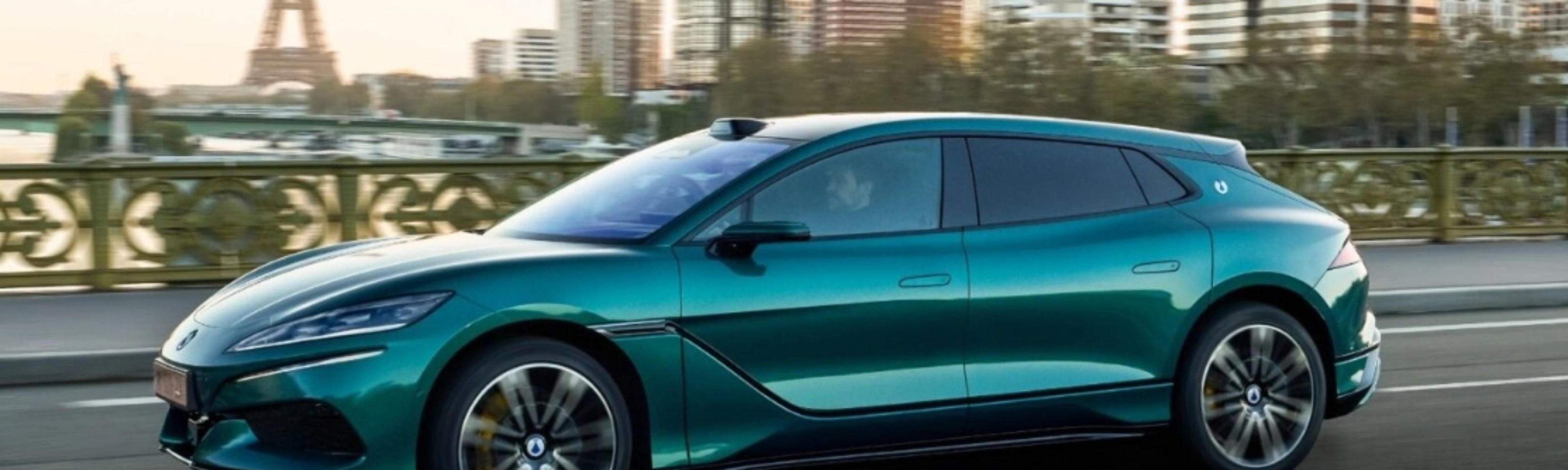Turquoise BYD electric car driving on a city road with a skyline in the background.