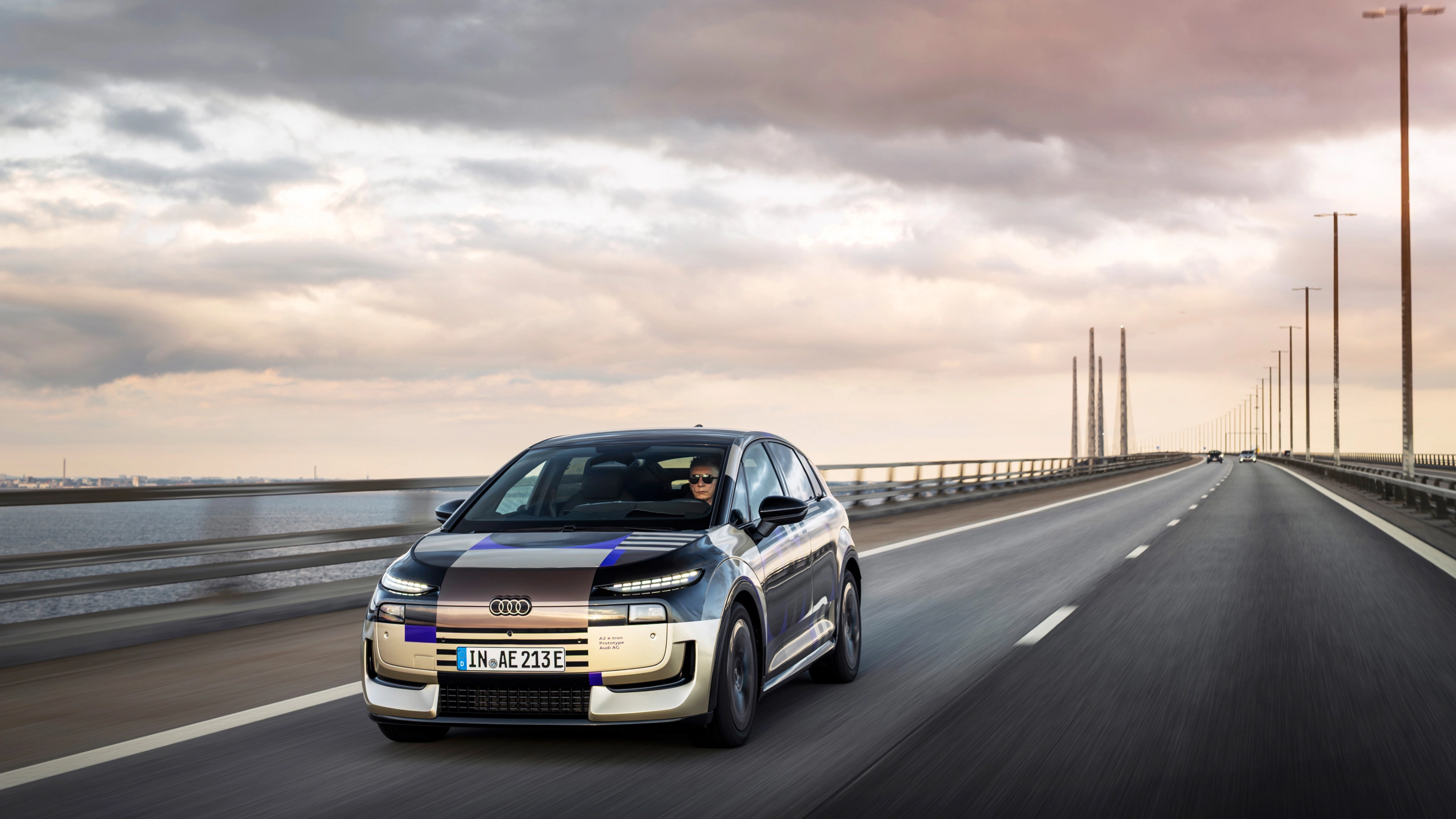 Audi prototype electric vehicle driving on an open road at sunset.
