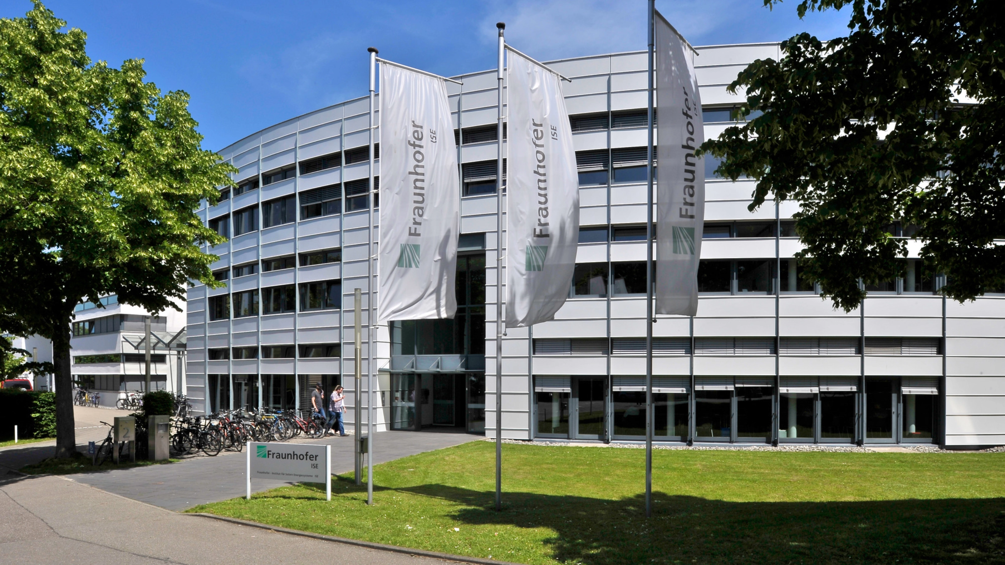 Modernes Fraunhofer-Institutsgebäude mit Fahnen und Bäumen davor.