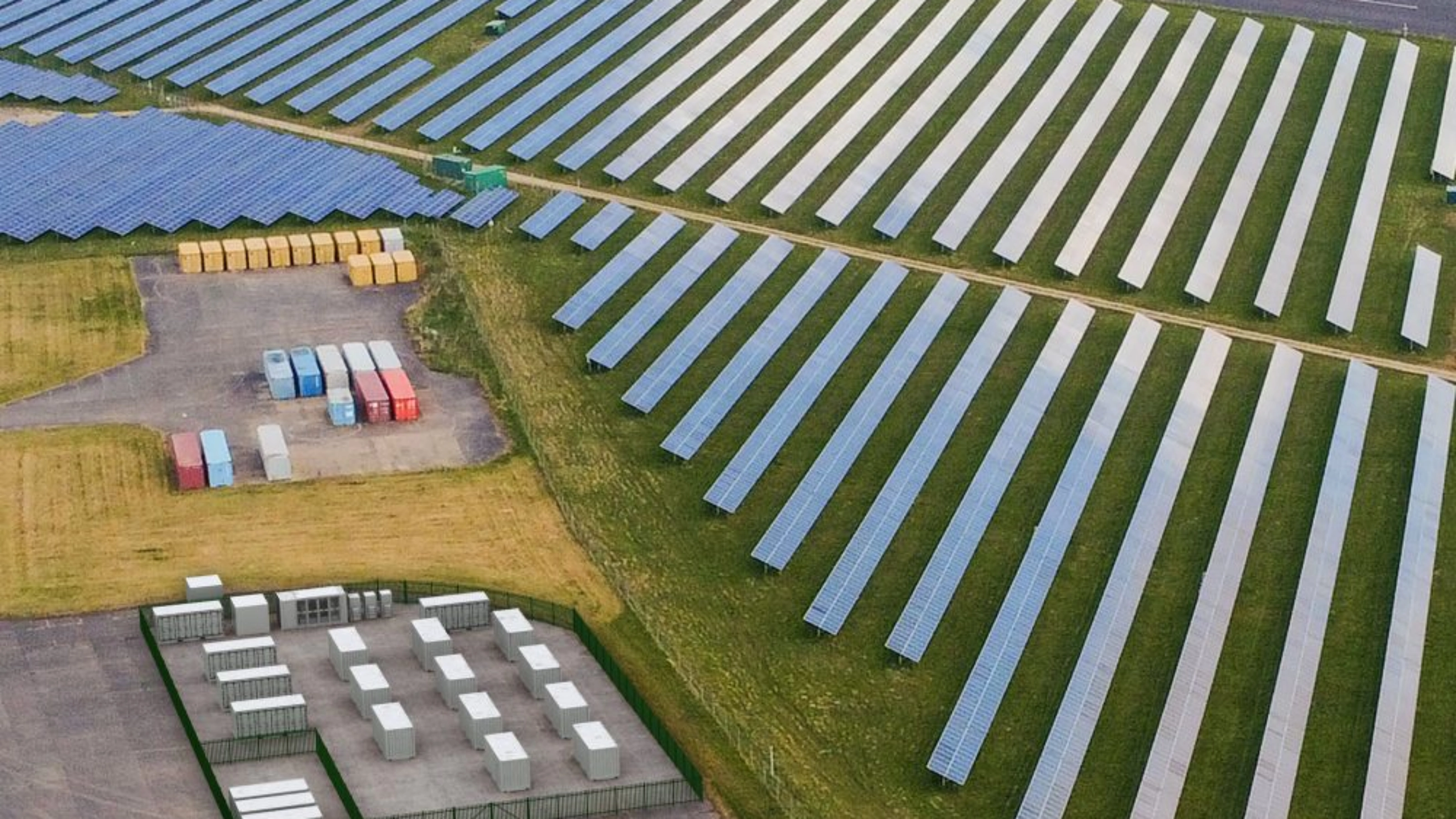 Luftaufnahme einer Solaranlage mit Reihen von Solarpaneelen und mehreren Containern.