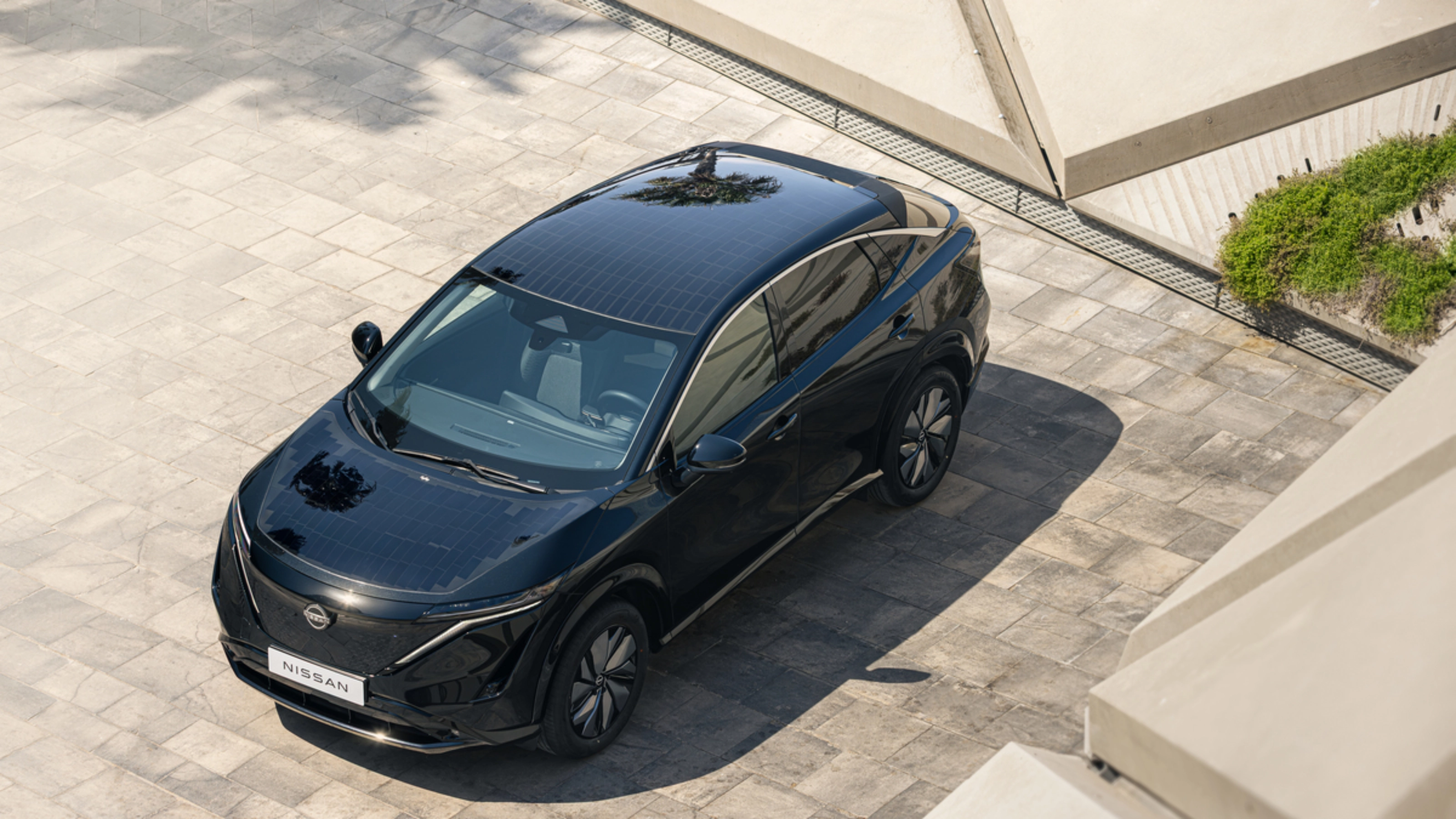 Ein schwarzes Elektro-SUV von Nissan steht auf einer gepflasterten Fläche im Sonnenlicht.
