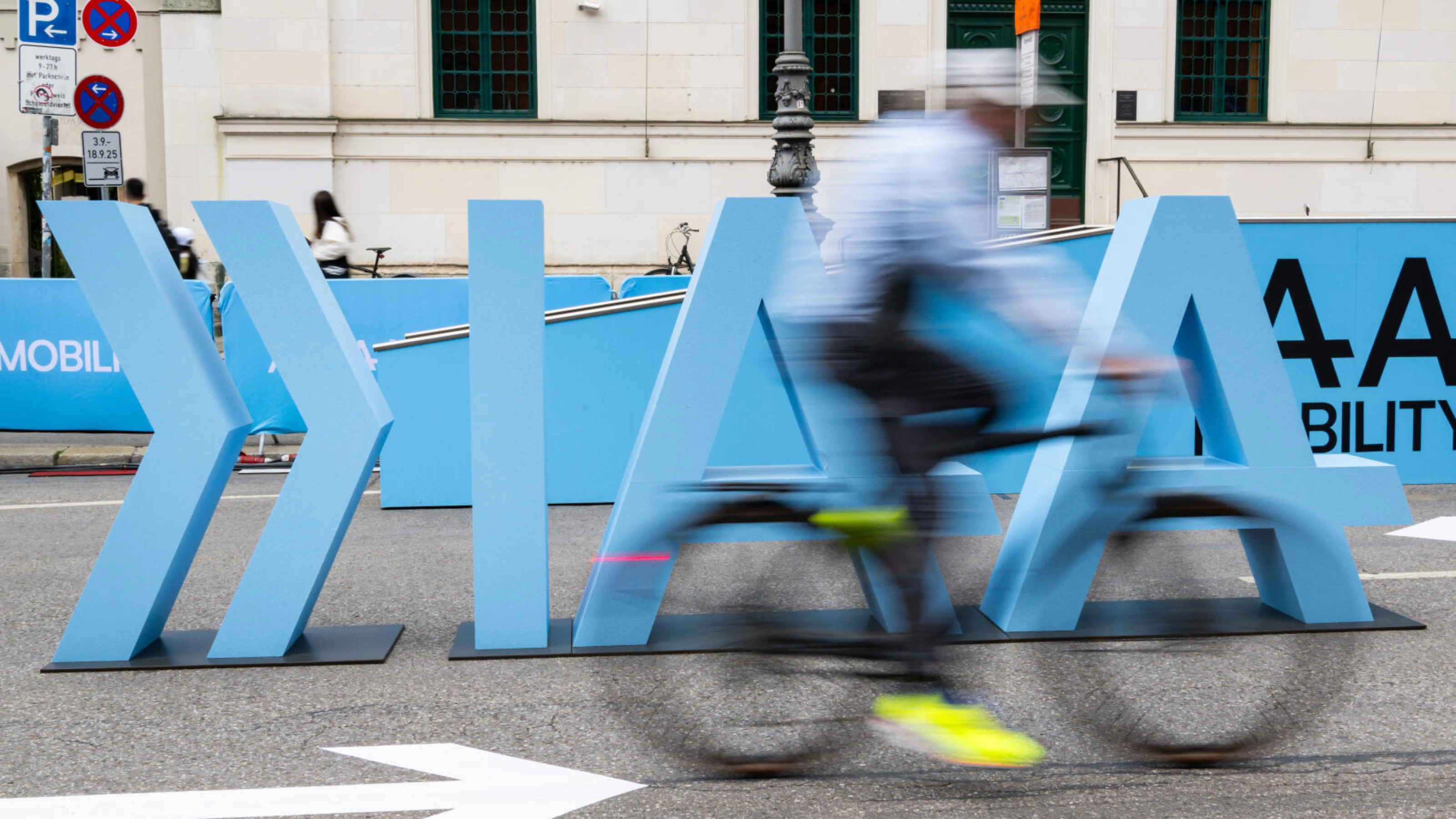 Cyclist rides past large IAA Mobility lettering on a city street.