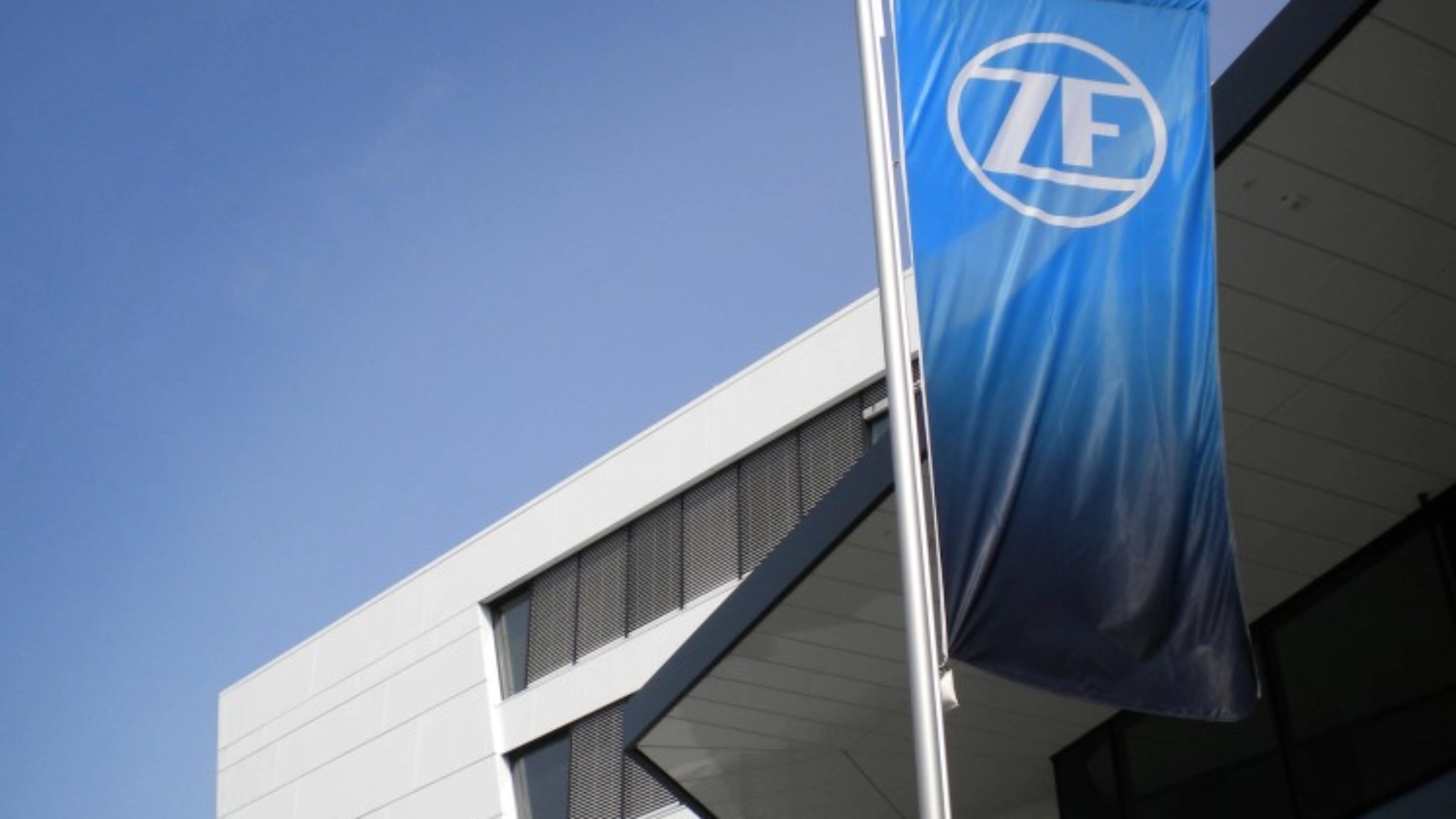 Blaue ZF-Flagge vor einem modernen Bürogebäude mit weißer Fassade.