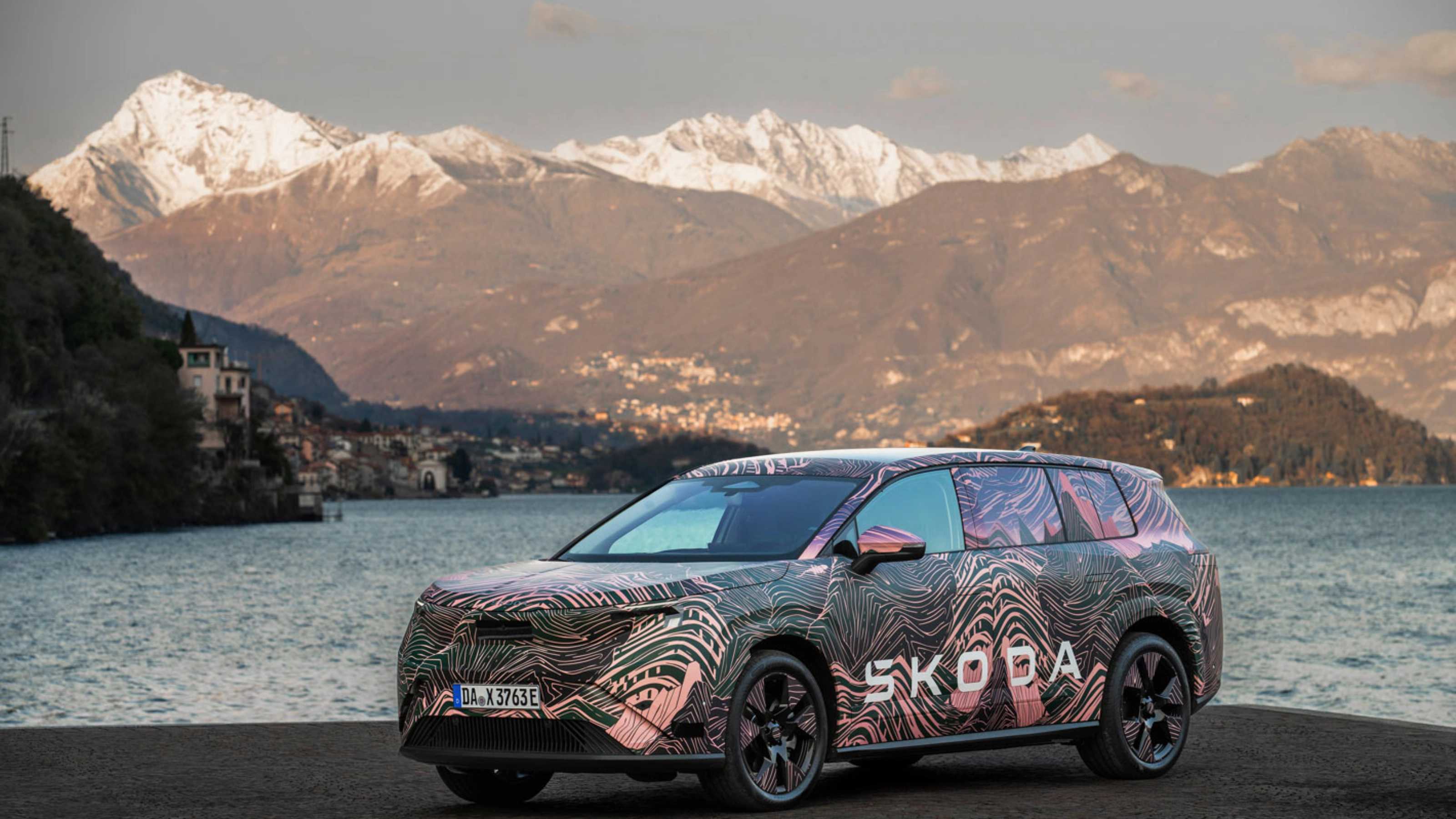 Getarnter Škoda steht am See vor schneebedeckten Bergen.
