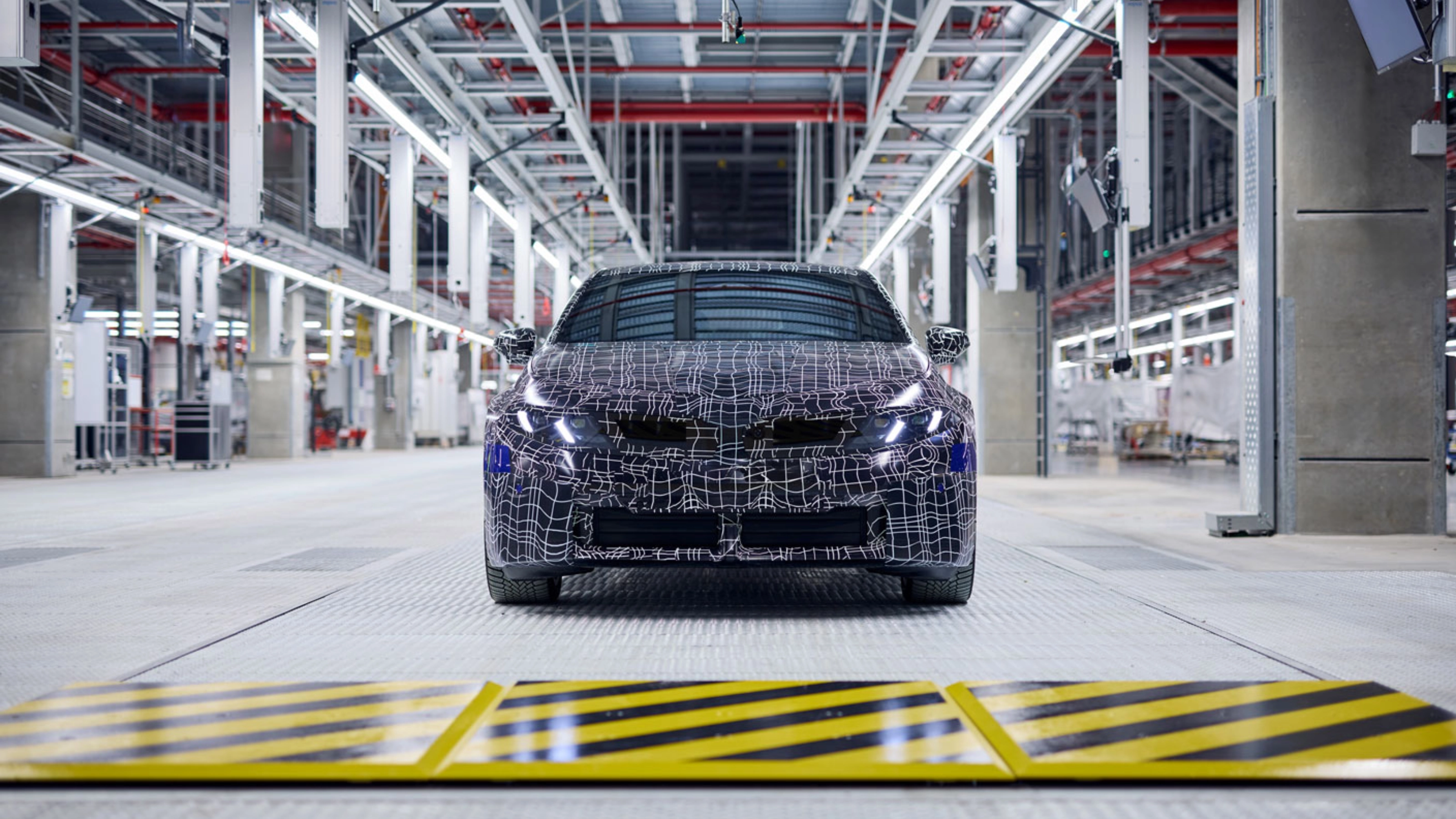 Ein getarntes Auto-Prototyp steht in einer hell beleuchteten Fahrzeugproduktionshalle.